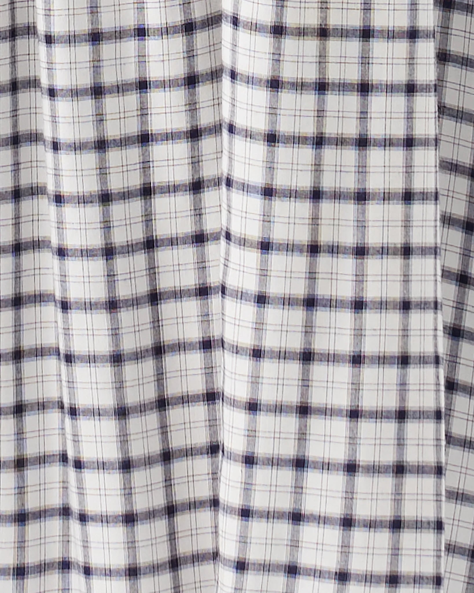 A close-up of a white fabric with a navy blue and thin gray plaid pattern, showing soft vertical folds.