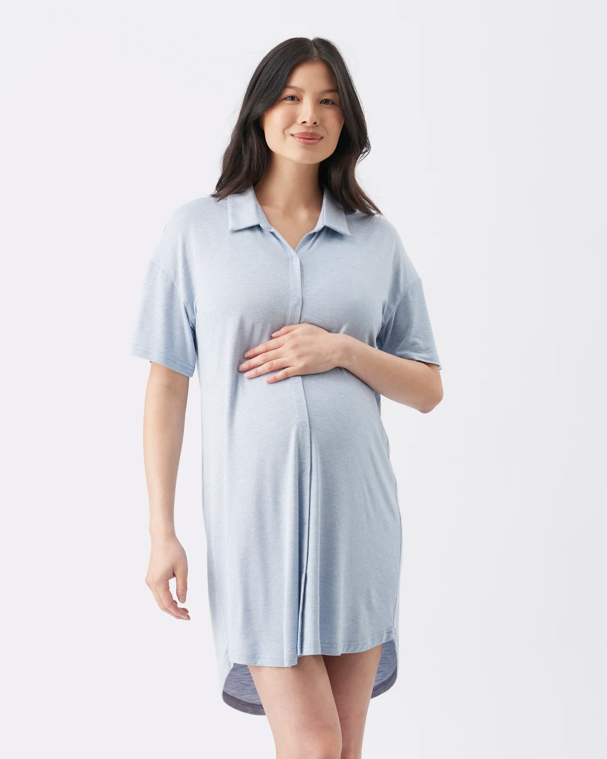 A pregnant woman wearing a light blue short-sleeve maternity shirt dress, standing against a plain white studio background.