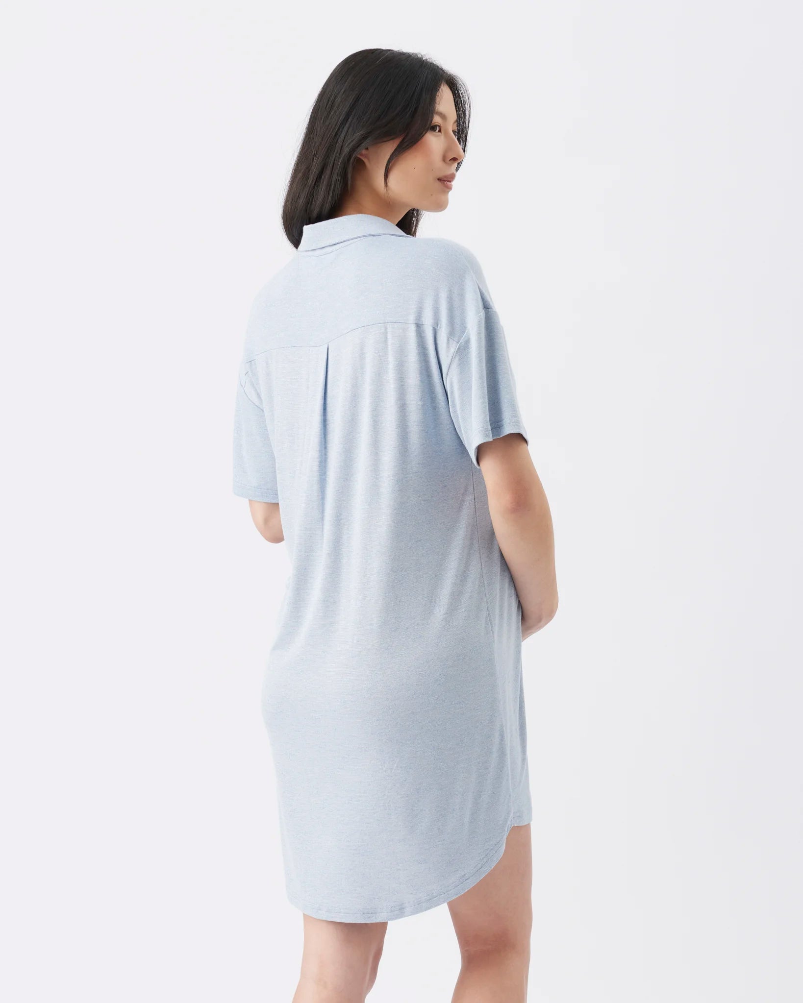 A woman wearing a light blue short-sleeve polo shirt dress, shown from the back against a plain white studio background.