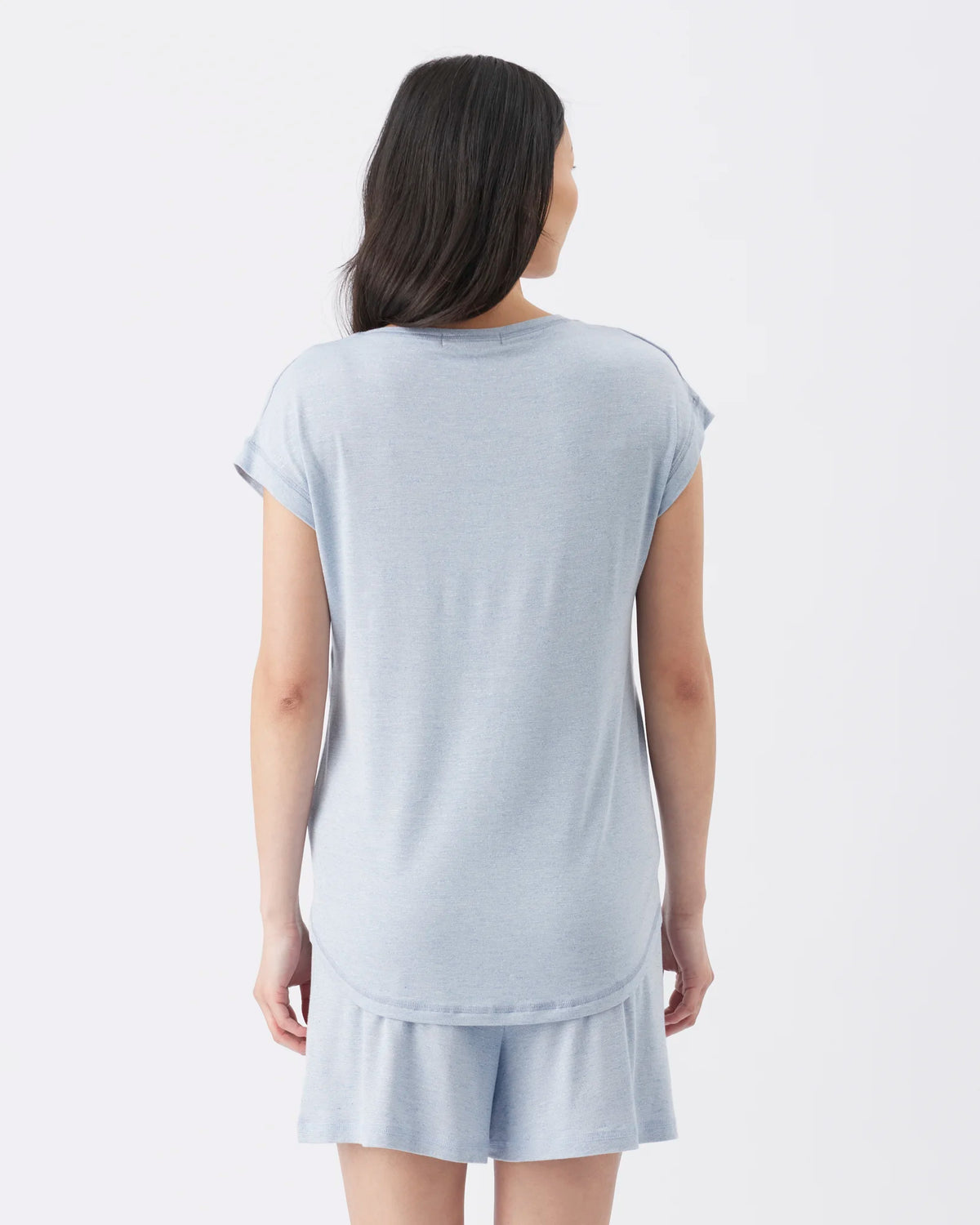 A woman viewed from the back wearing a light blue short-sleeve t-shirt and matching shorts against a plain white studio background.