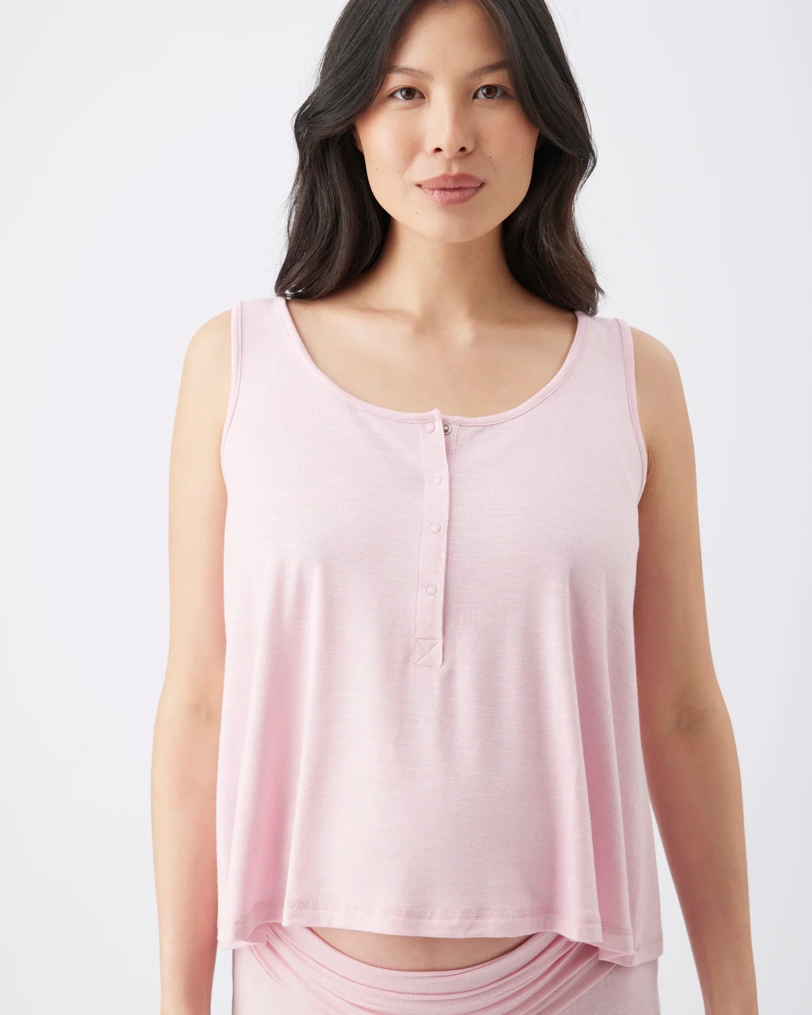 A woman wearing a light pink sleeveless henley tank top with a scoop neckline and small front buttons, shown against a plain light gray studio background.