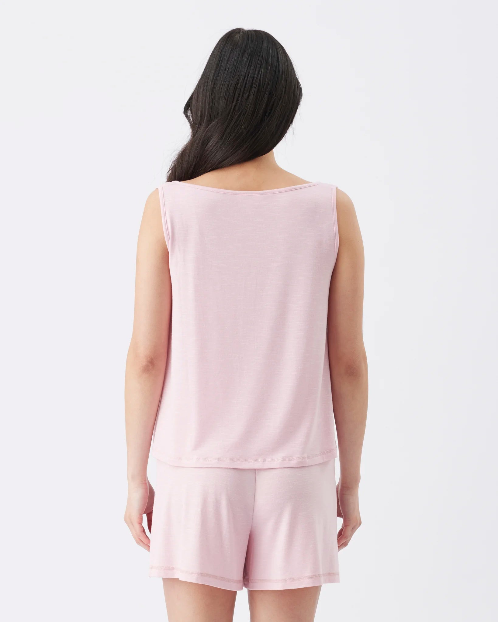 A woman viewed from the back wearing a light pink sleeveless top and matching shorts against a plain white studio background.