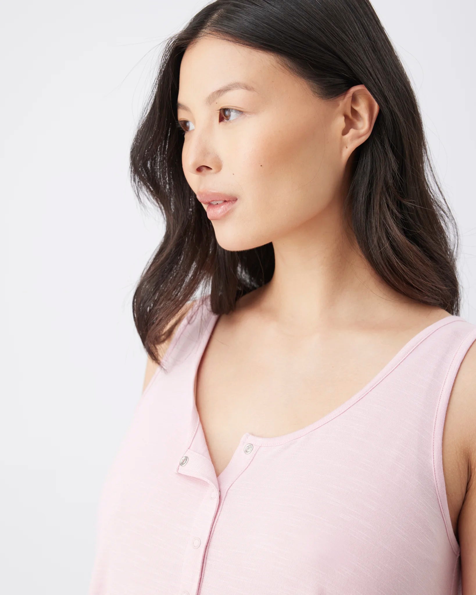 A woman with dark hair wearing a light pink sleeveless henley top, shown in a close-up profile against a plain light gray background.