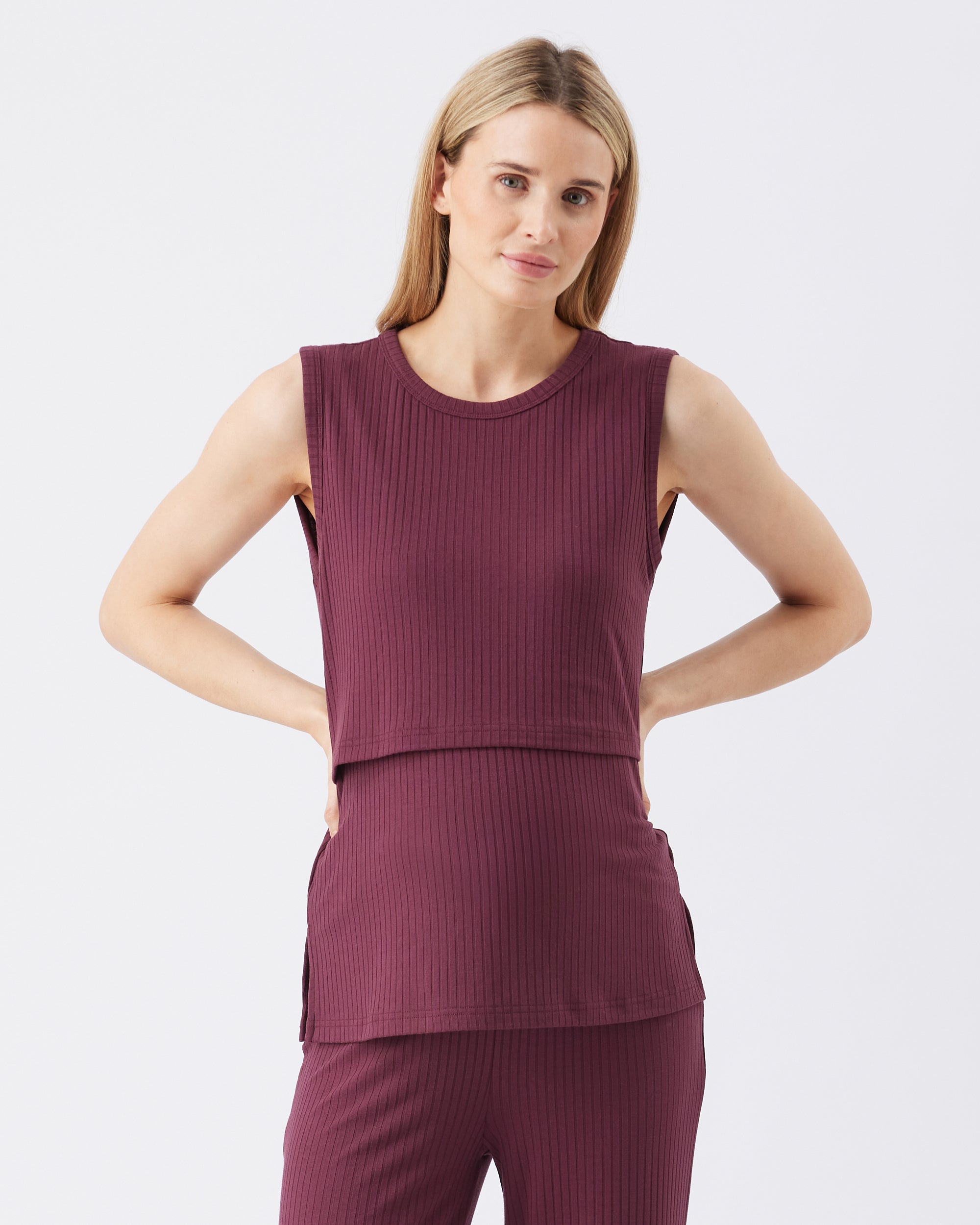 Woman wearing a maroon sleeveless top and pants on a white background