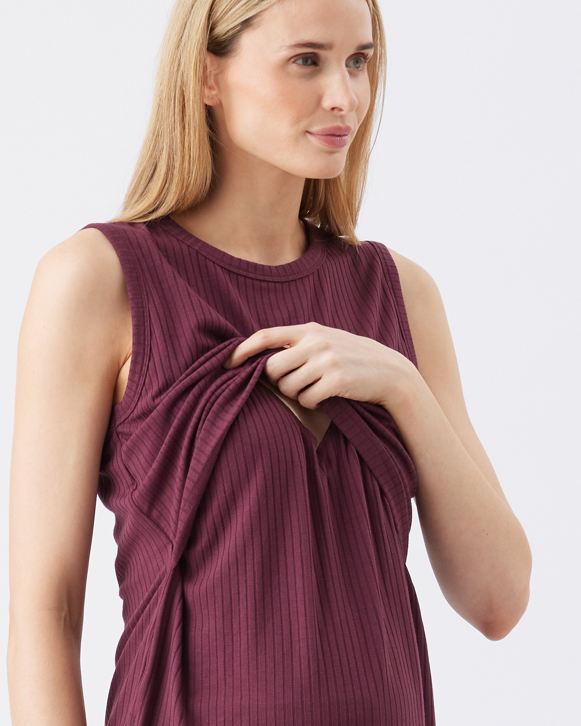 Woman showing the nursing access while wearing a maroon sleeveless top against a white background