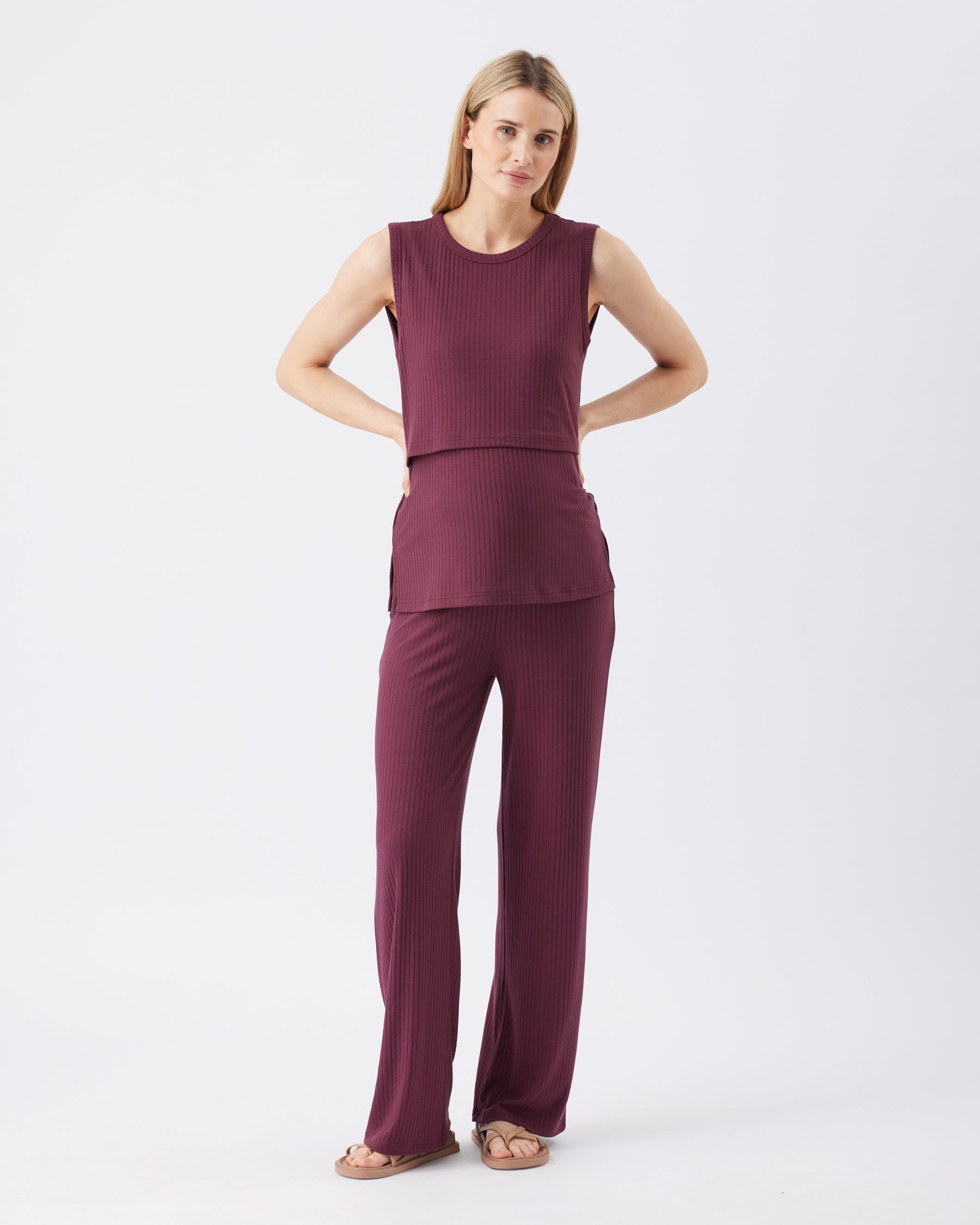 Full length shot of a woman wearing a burgundy sleeveless top and pants on a white background