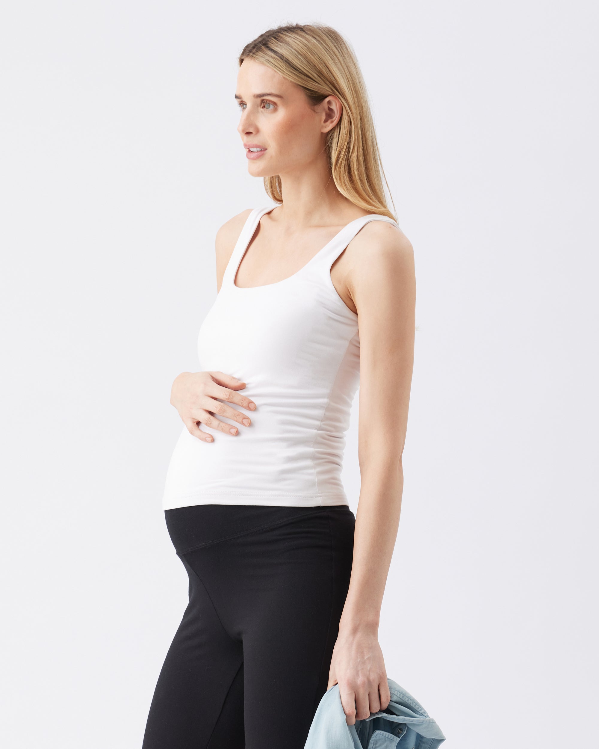 Woman wearing a white tank top and black pants on a light gray background