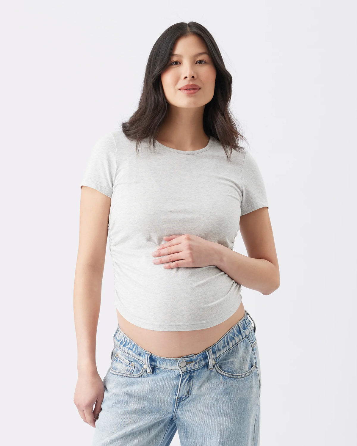 A woman modeling a light gray short-sleeve crop top and light blue jeans against a plain white studio background.