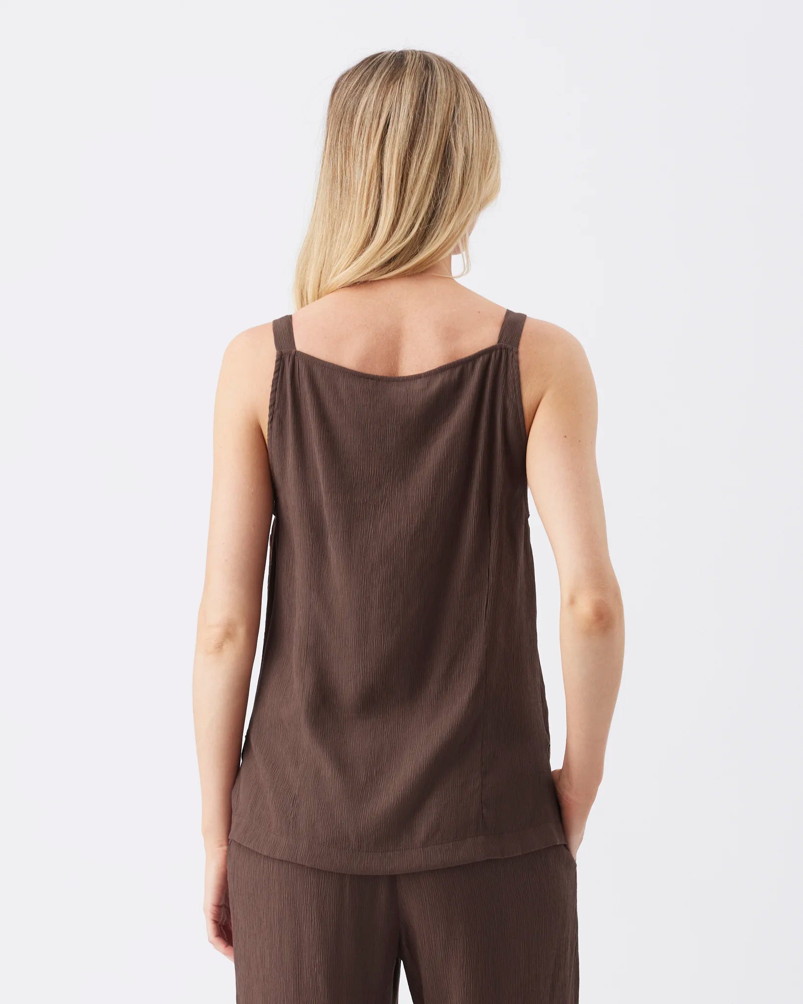 A woman shown from the back wearing a dark brown sleeveless top and matching brown bottoms against a plain light gray studio background.