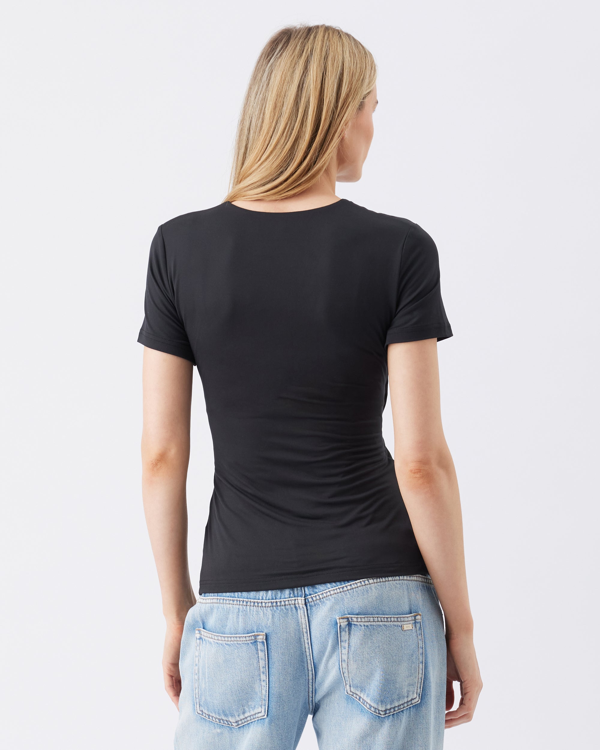 Back view of a woman wearing a black t-shirt and blue jeans on a white background