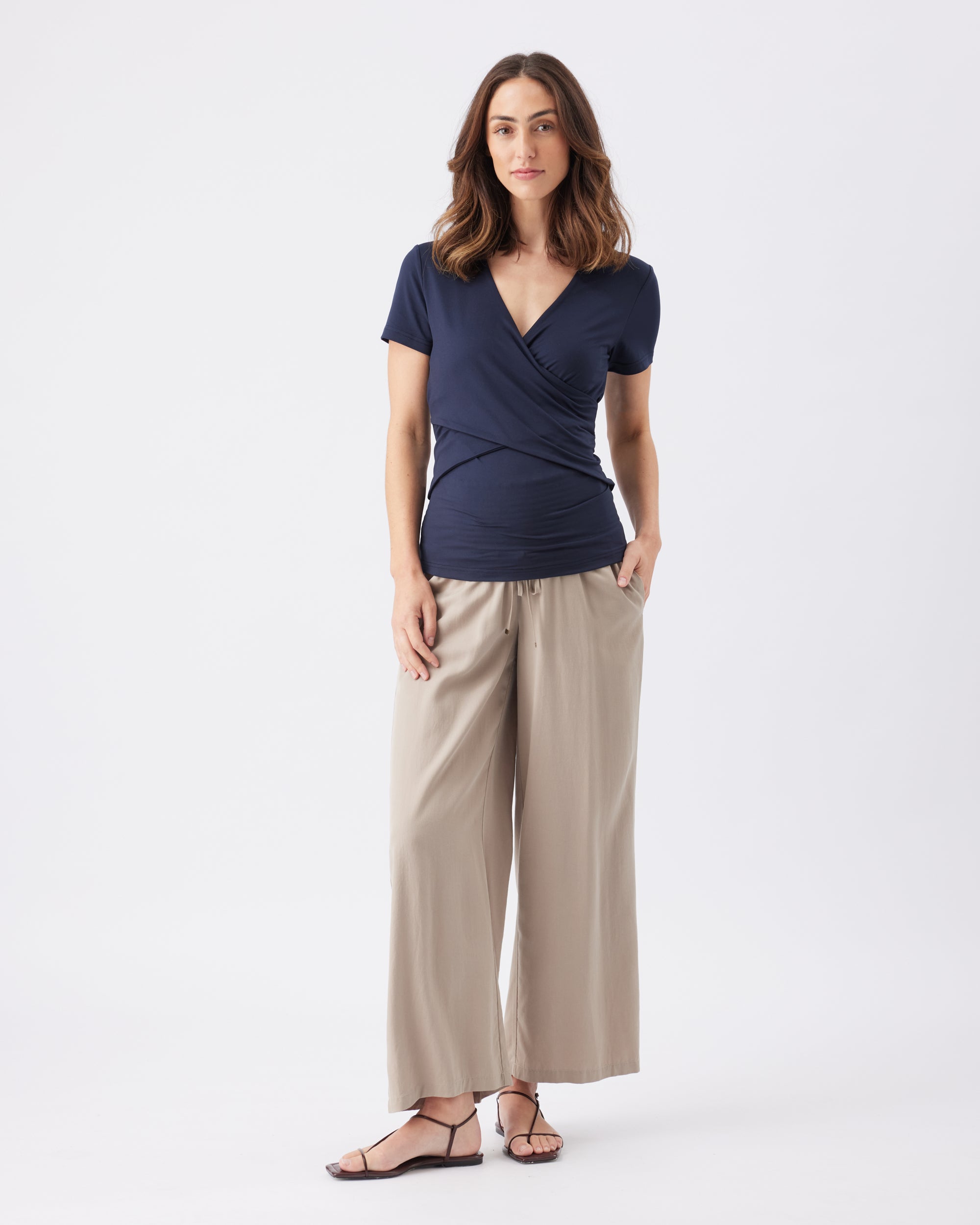 Full length shot of a woman wearing a navy top and beige pants on a white background