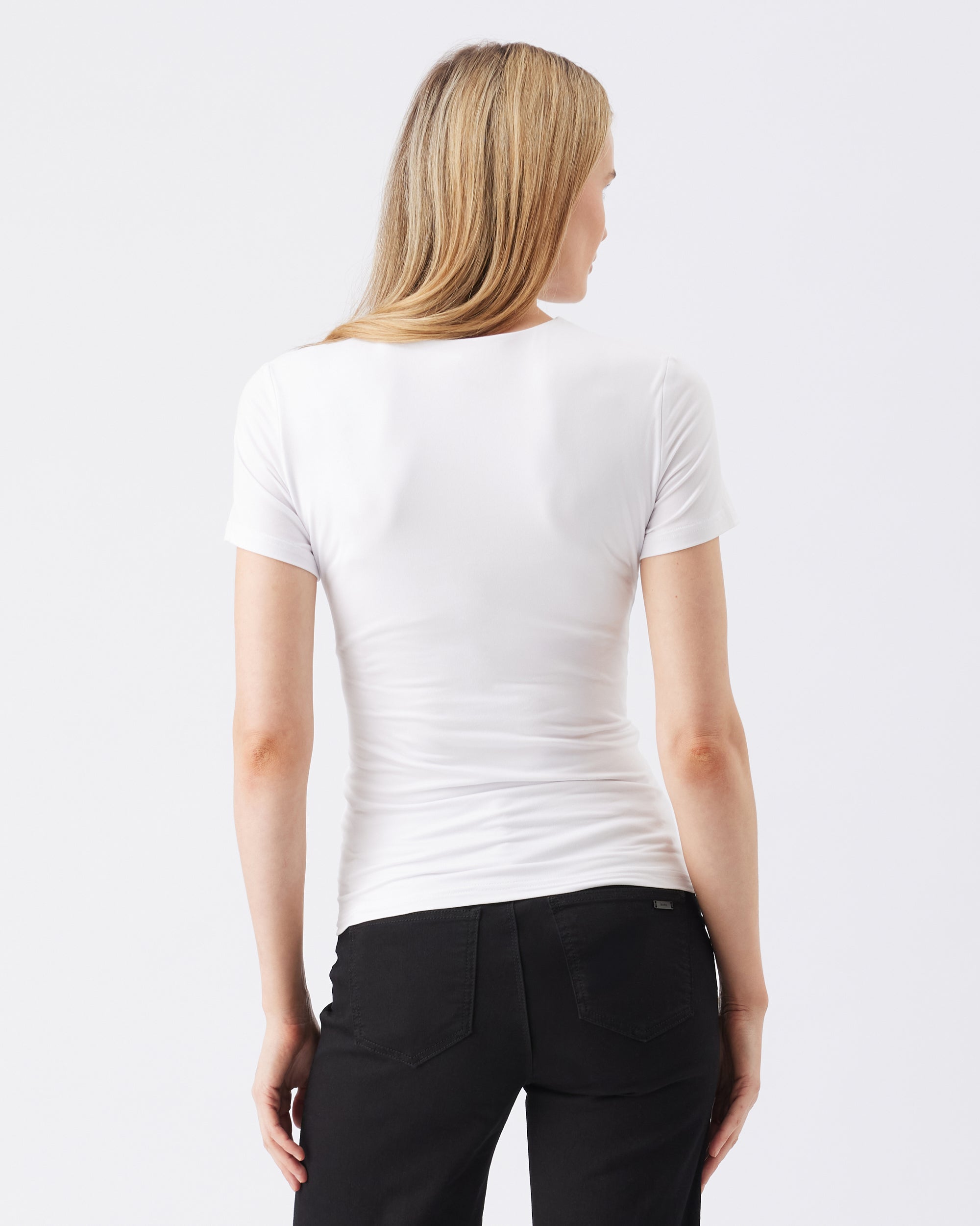 Back view of a woman wearing a white t-shirt and black pants on a plain background