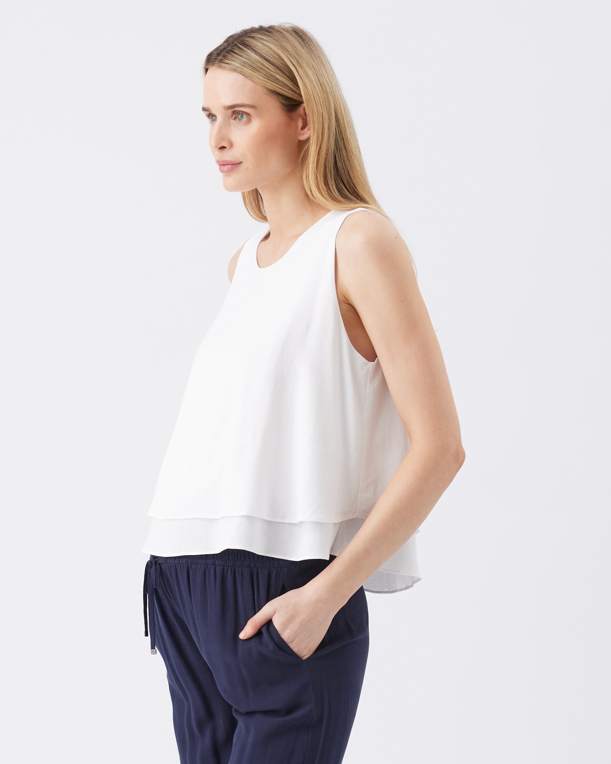 Pregnant woman wearing a white sleeveless top and navy pants on a light gray background