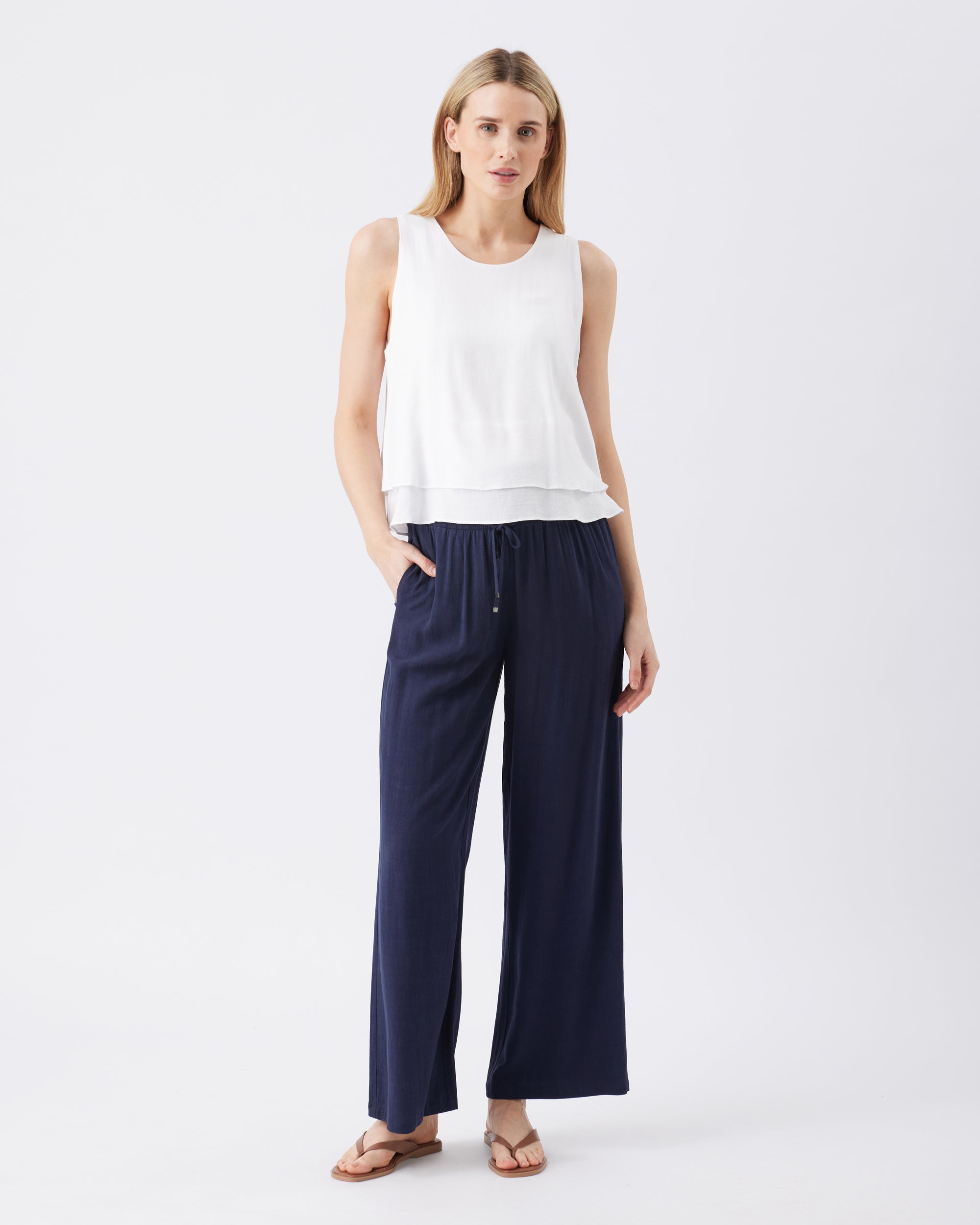 Woman wearing a white sleeveless top and navy wide-leg pants on a white background