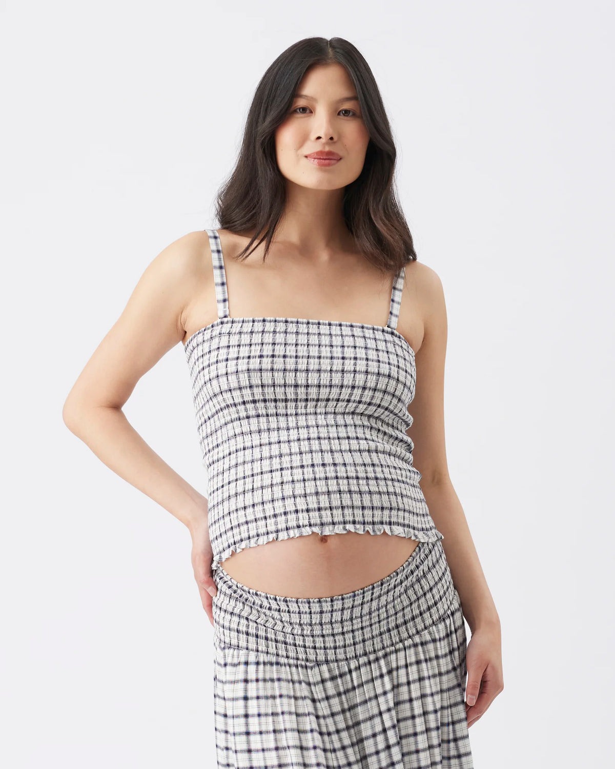 A woman modeling a black and white checkered two-piece set consisting of a cropped camisole top and matching high-waisted shorts, against a plain light gray background.