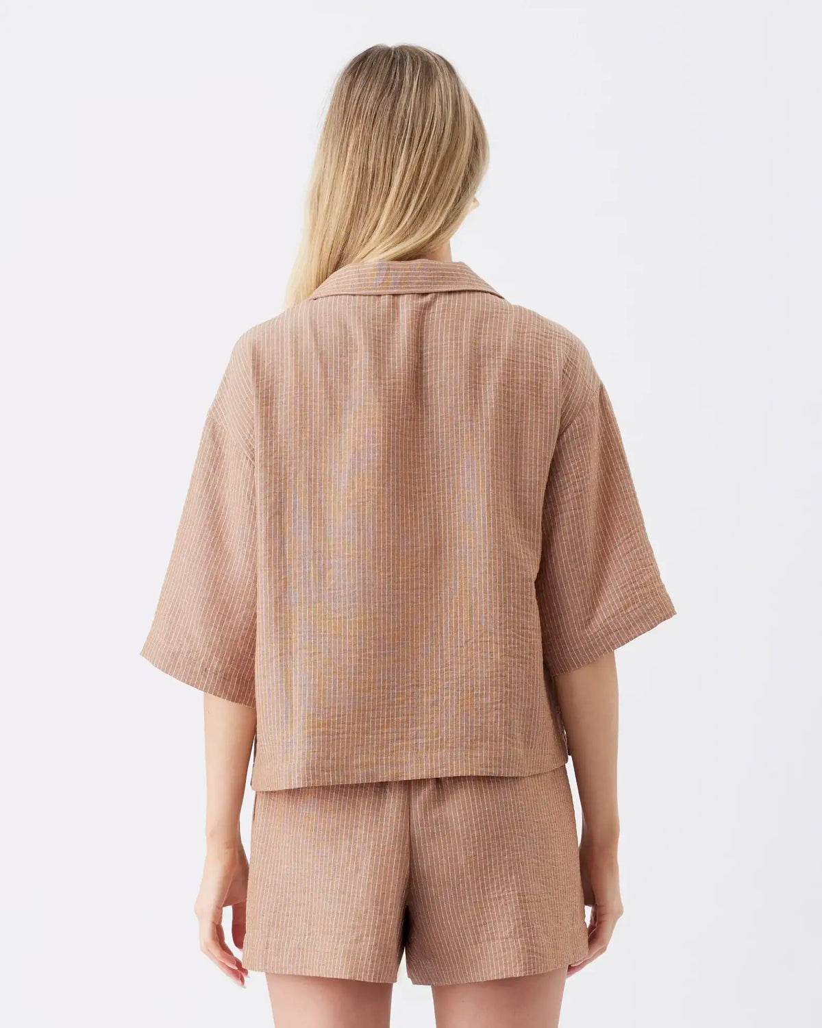 A woman shown from the back wearing a matching beige textured short-sleeve button-up shirt and shorts set against a plain white studio background.