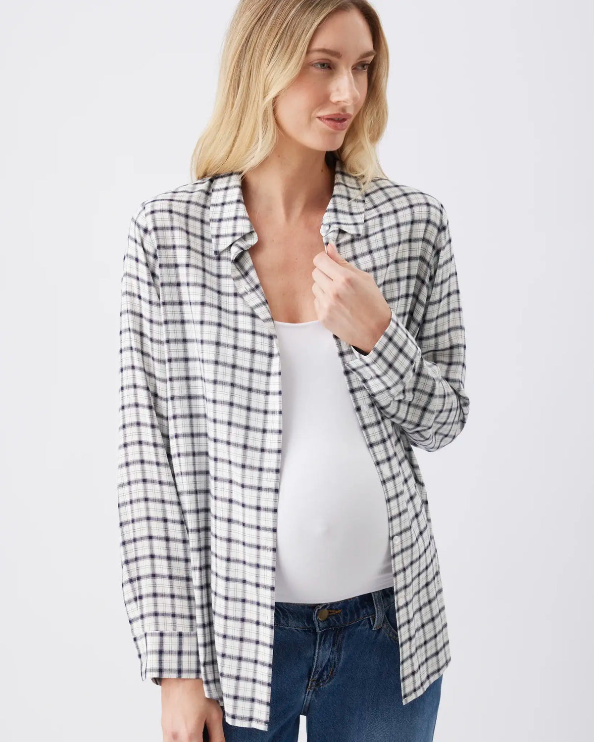 A pregnant woman wearing a black and white checkered plaid button-up shirt over a white tank top and blue jeans, photographed against a light gray studio background.