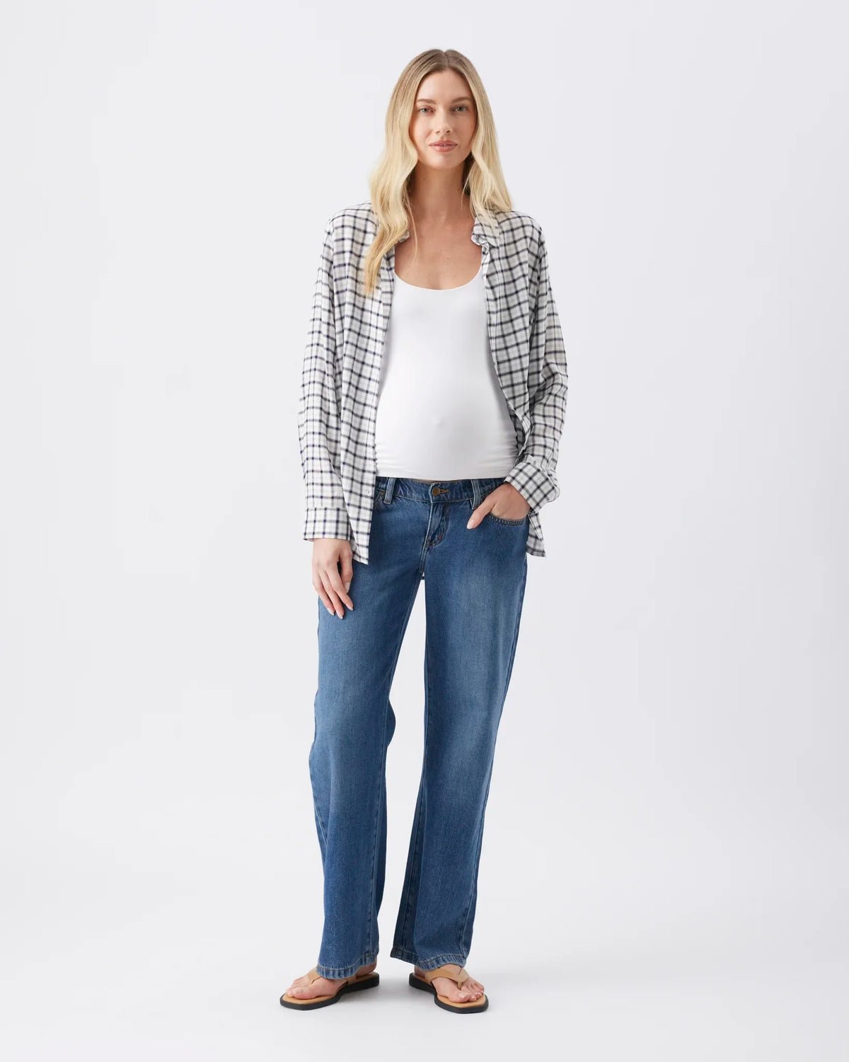 A woman modeling a black and white checkered button-up shirt over a white tank top and blue jeans, standing against a plain white studio background.