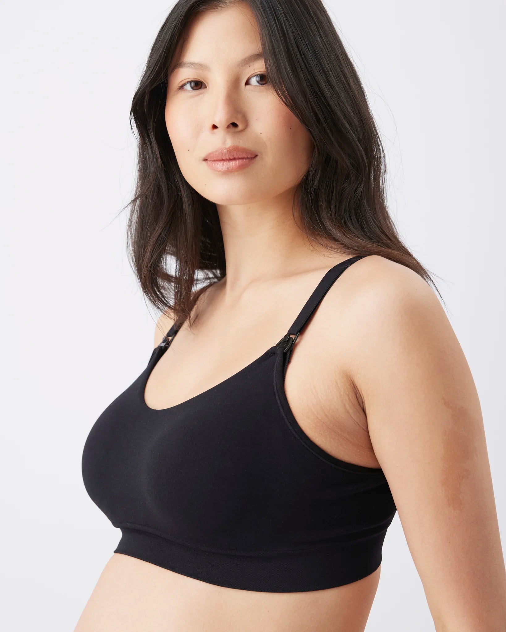 A woman wearing a black wireless bralette with thin adjustable shoulder straps, shown from the chest up against a plain light gray studio background.