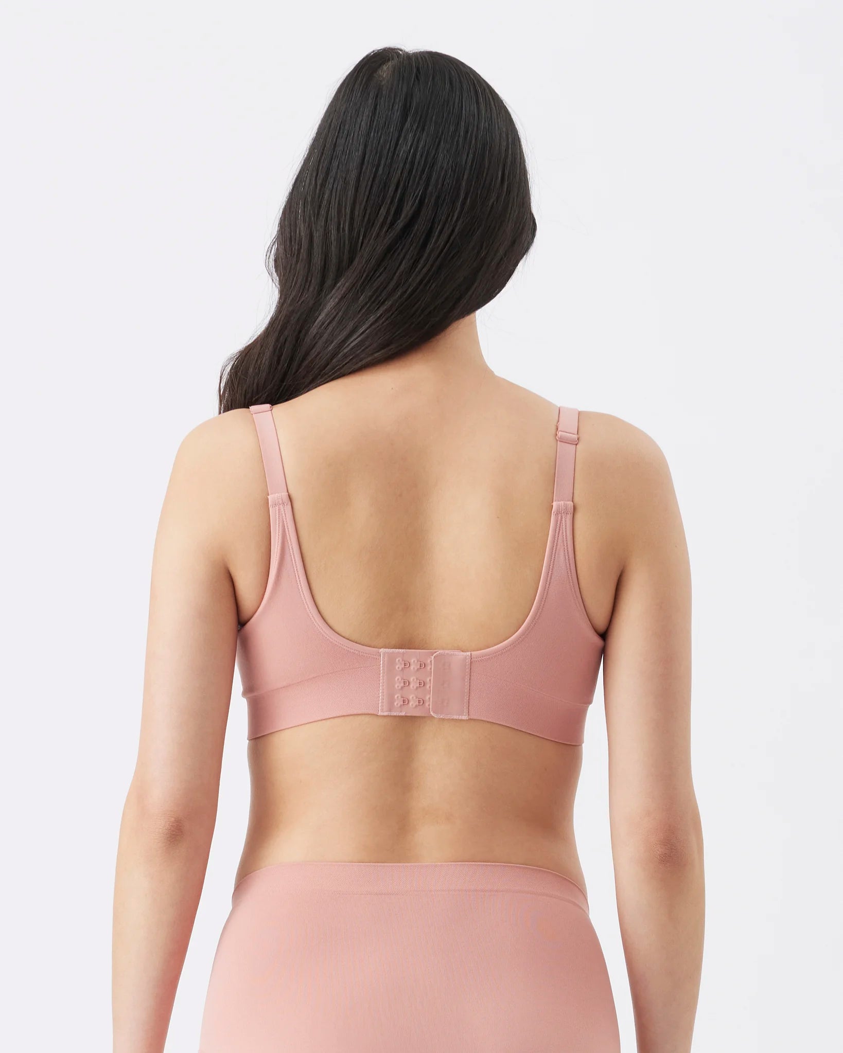 A woman shown from the back wearing a dusty pink bra and matching underwear against a light gray studio background.