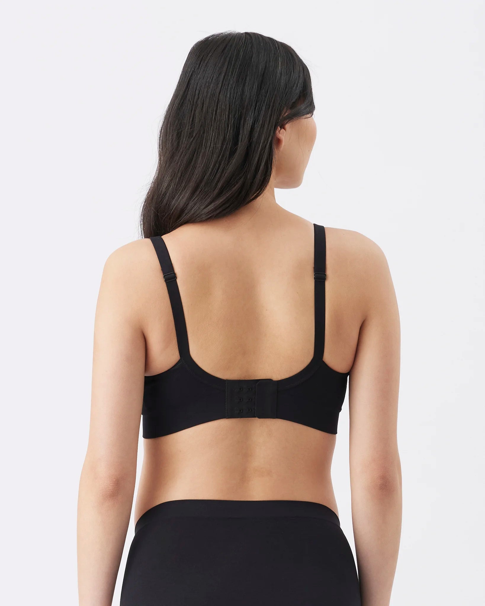 A woman shown from the back wearing a black bra and black bottoms against a light gray studio background.