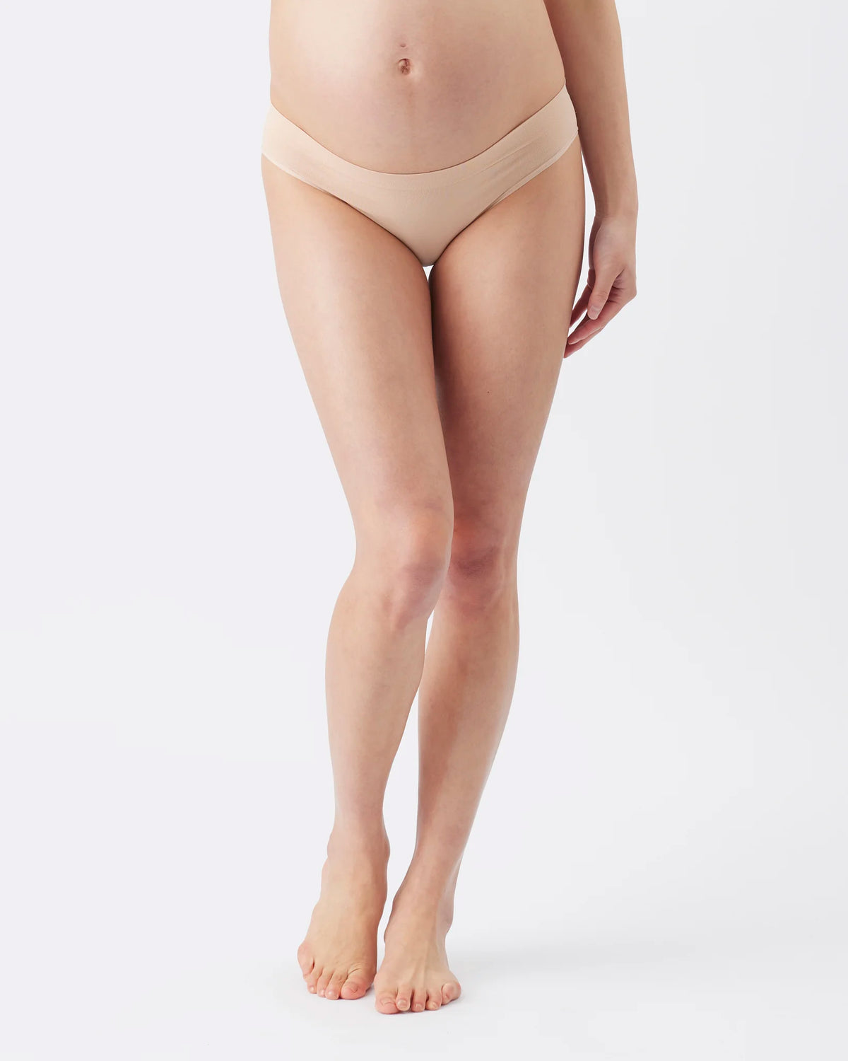 A model wearing a pair of high-waisted, low-rise maternity briefs in a nude beige color, shown from the waist down against a clean white studio background.