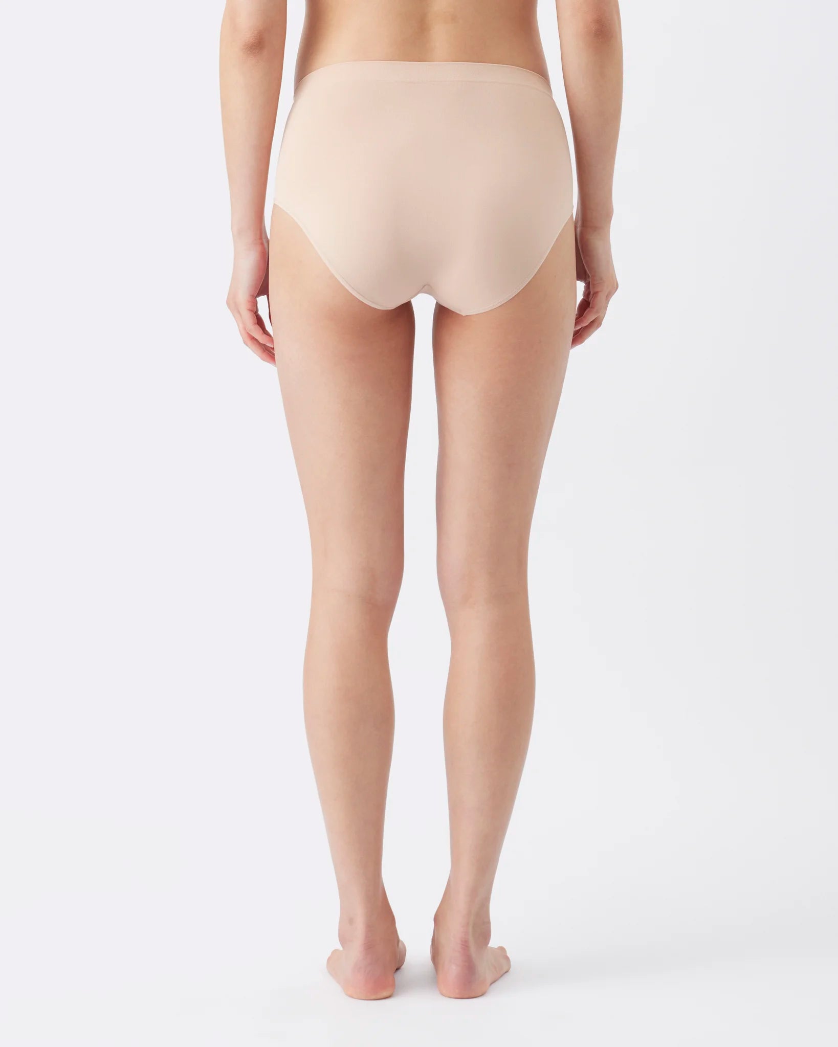 Rear view of a model wearing high-waisted, seamless shapewear briefs in a light beige shade against a plain white studio background.