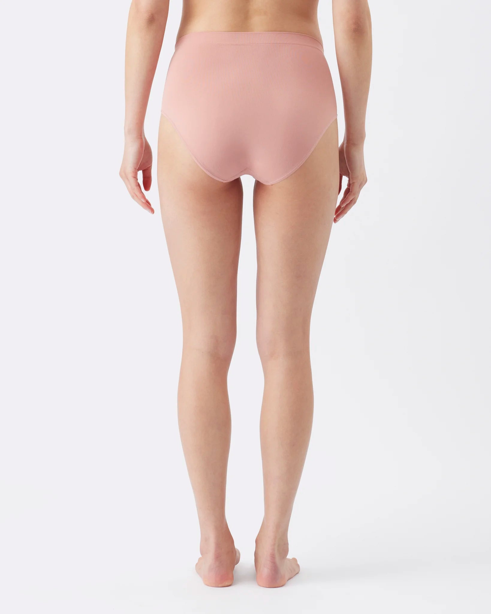 Rear view of a model wearing high-waisted, seamless underwear in a dusty rose pink color, photographed against a clean white studio background.