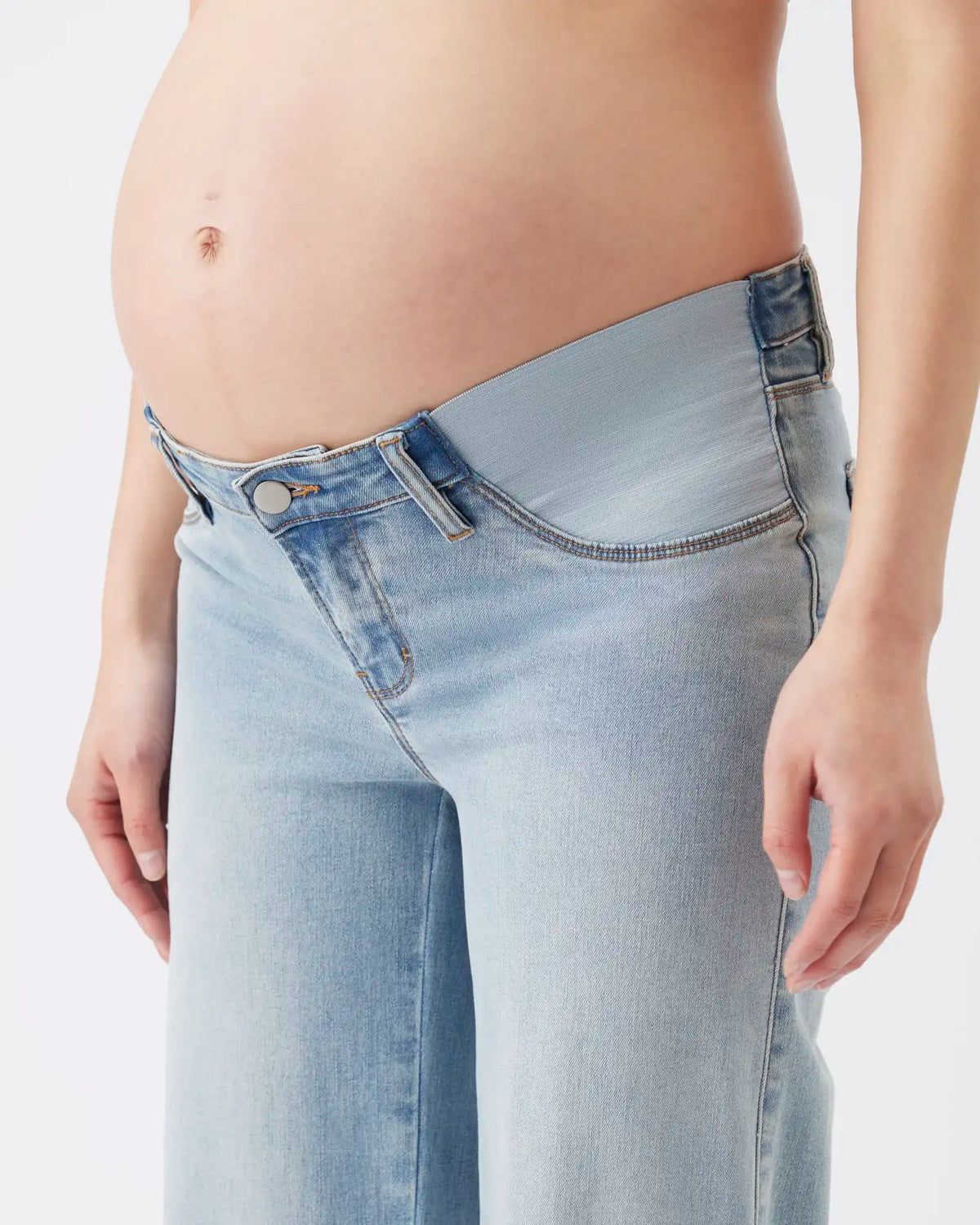 A close-up of a pregnant model wearing light-wash blue denim jeans with a wide, comfortable waistband and no visible belt loops.