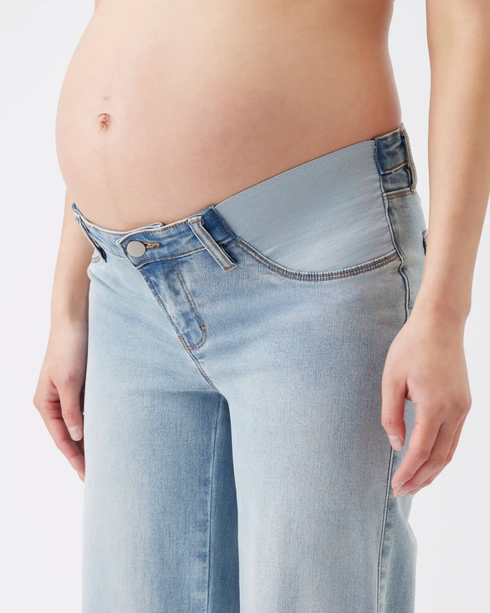 A close-up of a pregnant model wearing light-wash blue denim jeans with a wide, comfortable waistband and no visible belt loops.