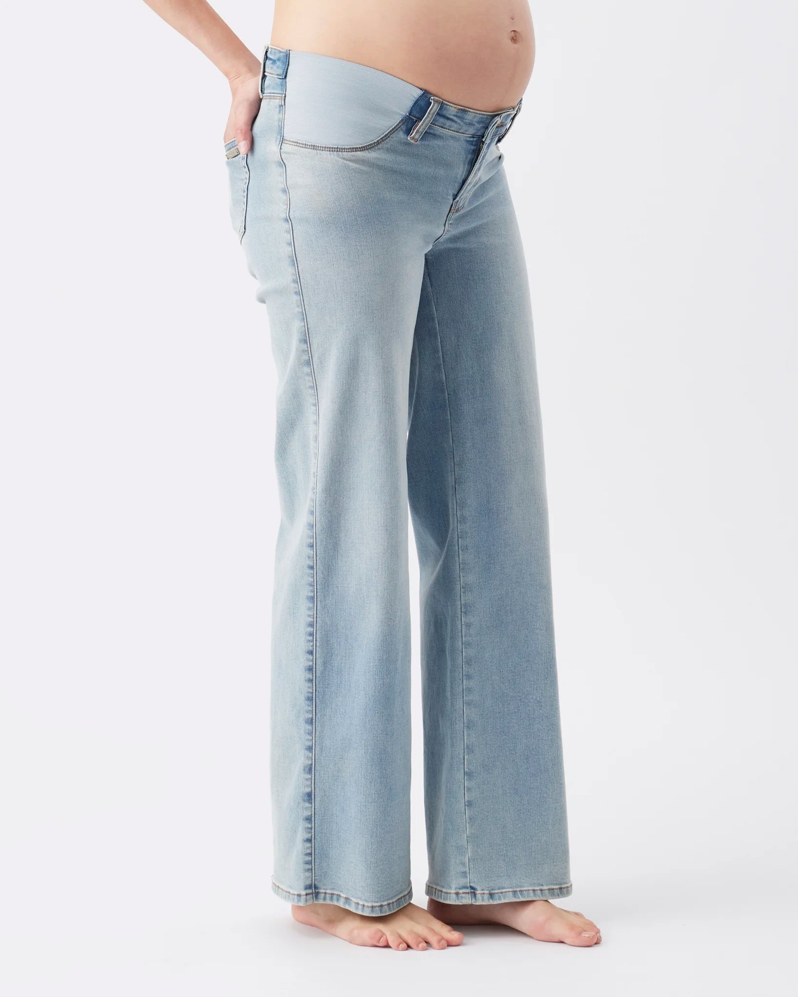 A pregnant model wearing light-wash, wide-leg denim jeans, shown from the waist down against a plain white studio background.