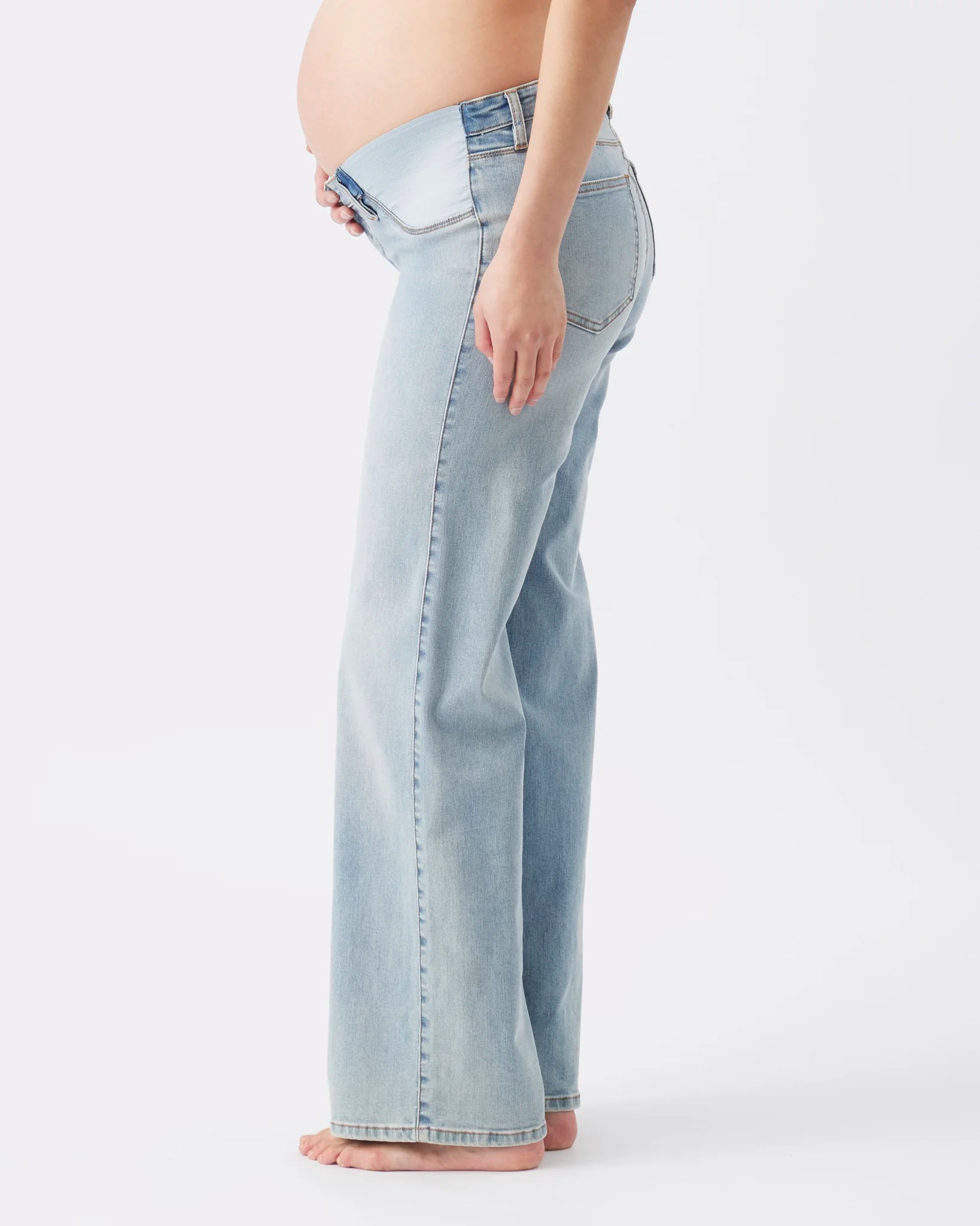 Side view of a pregnant model wearing light-wash blue flare jeans, showing the fit from the waist down against a plain white studio background.