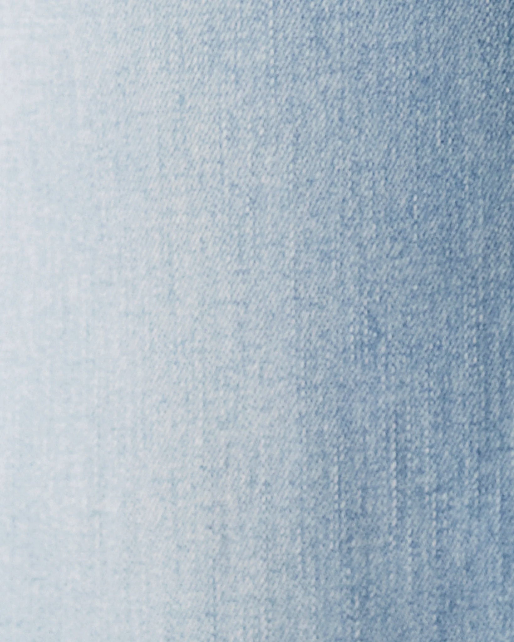A close-up of light blue denim fabric texture with a subtle gradient from pale blue on the left to a slightly deeper blue on the right.