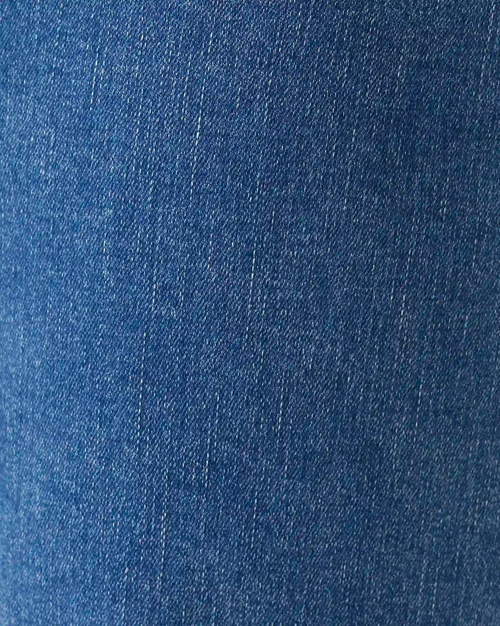 A close-up texture shot of blue denim fabric, showing the fine twill weave and subtle fading.
