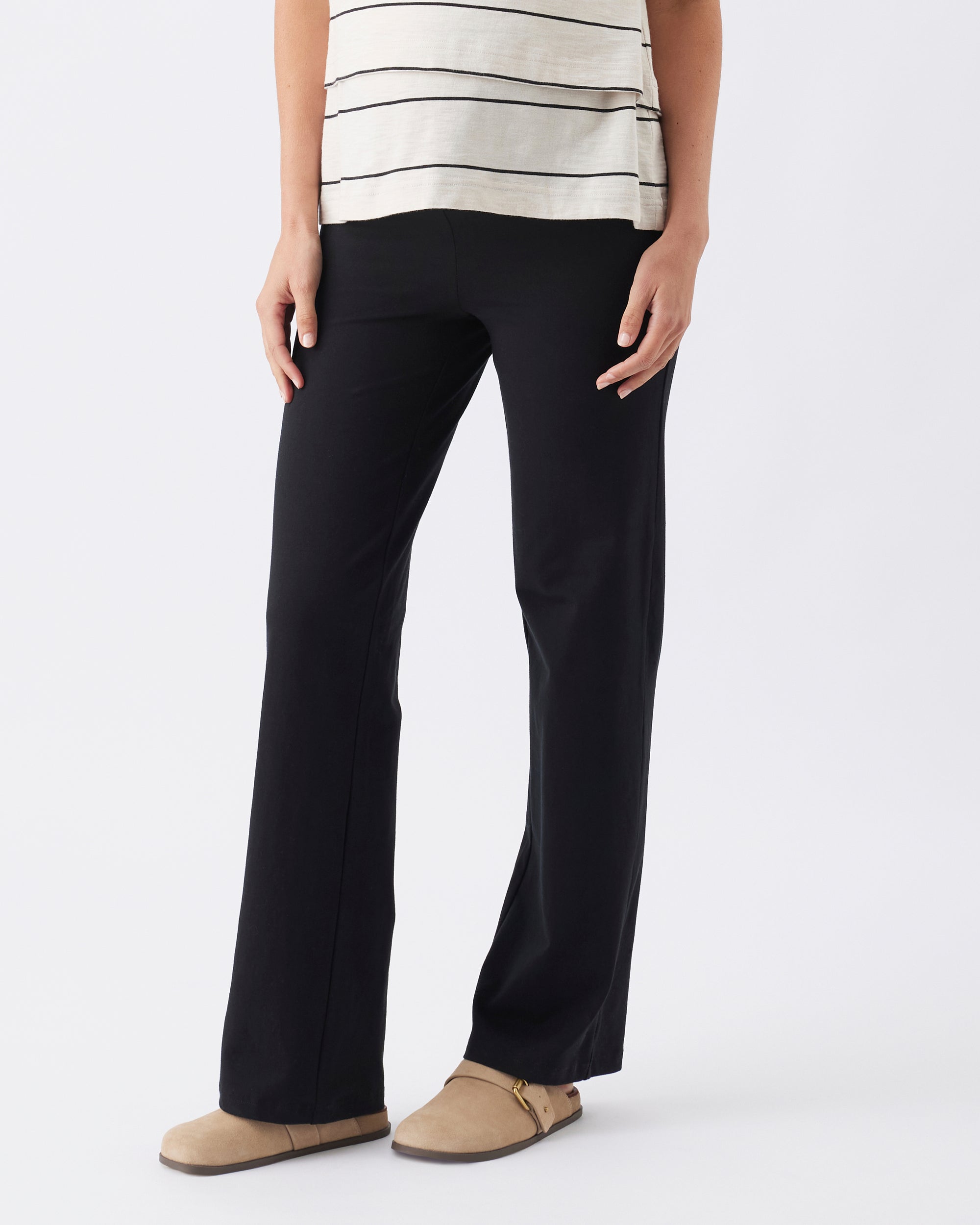 Person wearing straight leg black pants and a striped top on a white background