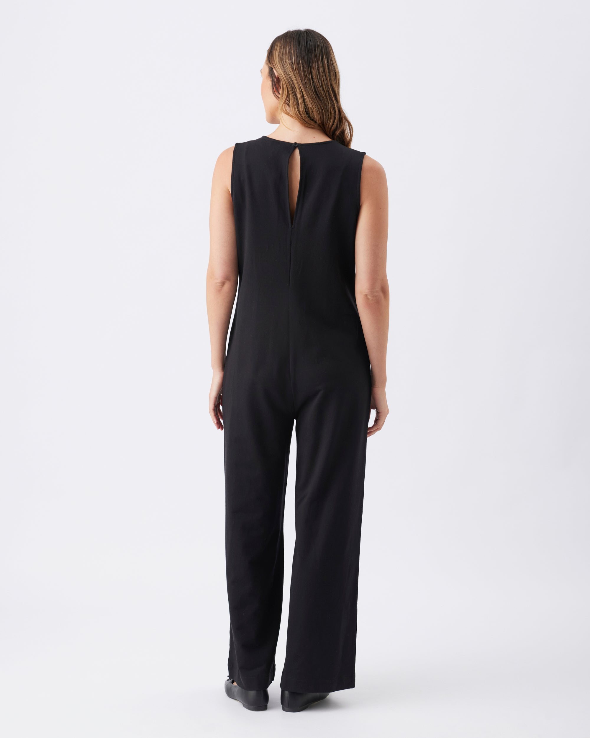Back view of a woman wearing a black full length jumpsuit with a keyhole back on a white background