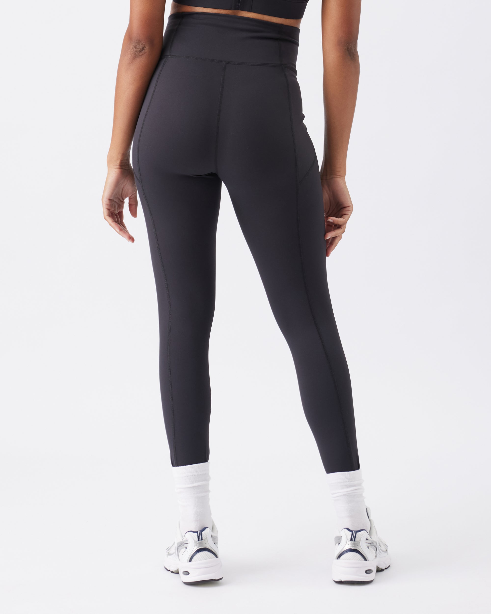 Back view of a woman wearing black leggings on a white background