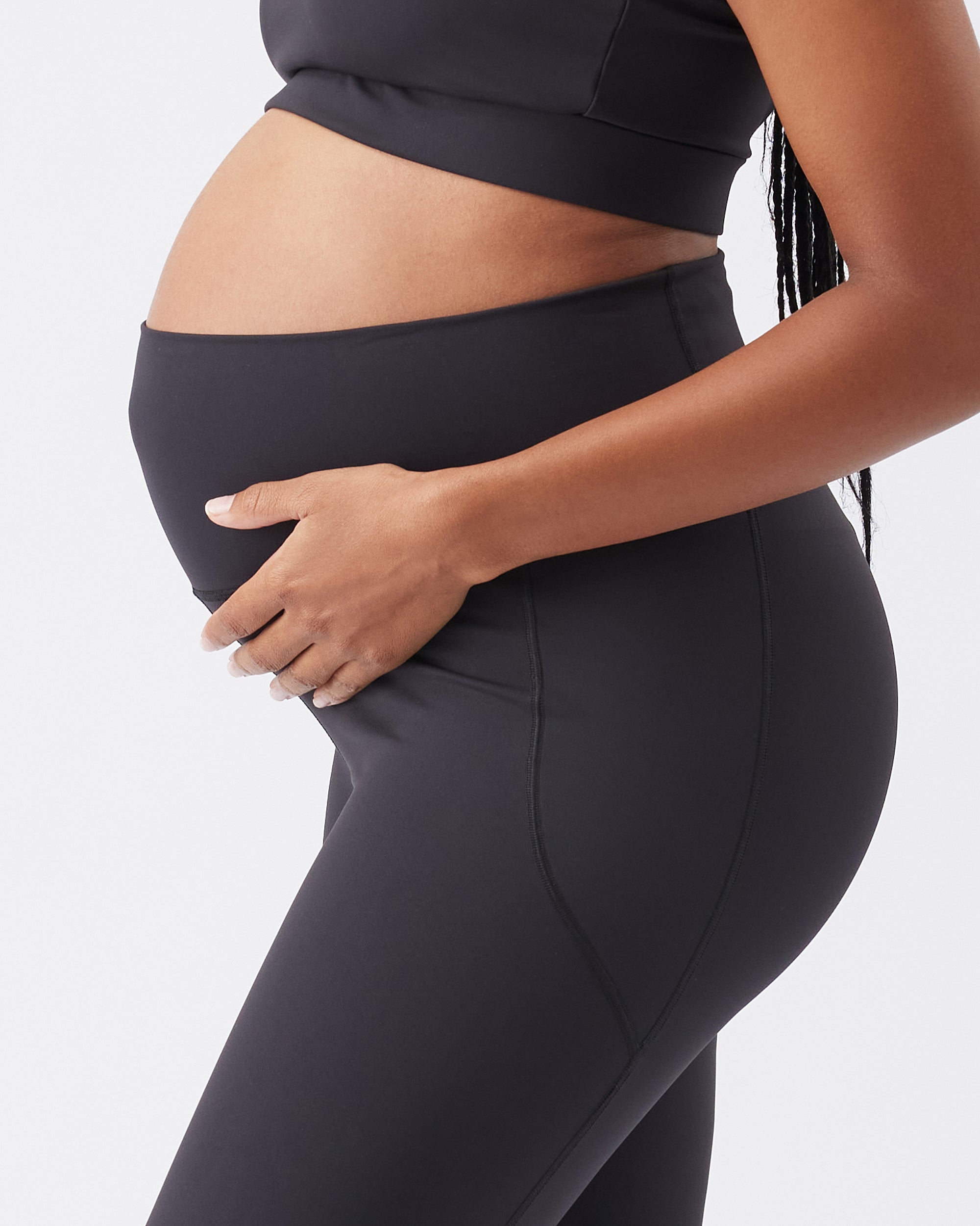 Close up of a pregnant woman wearing black leggings on a plain background