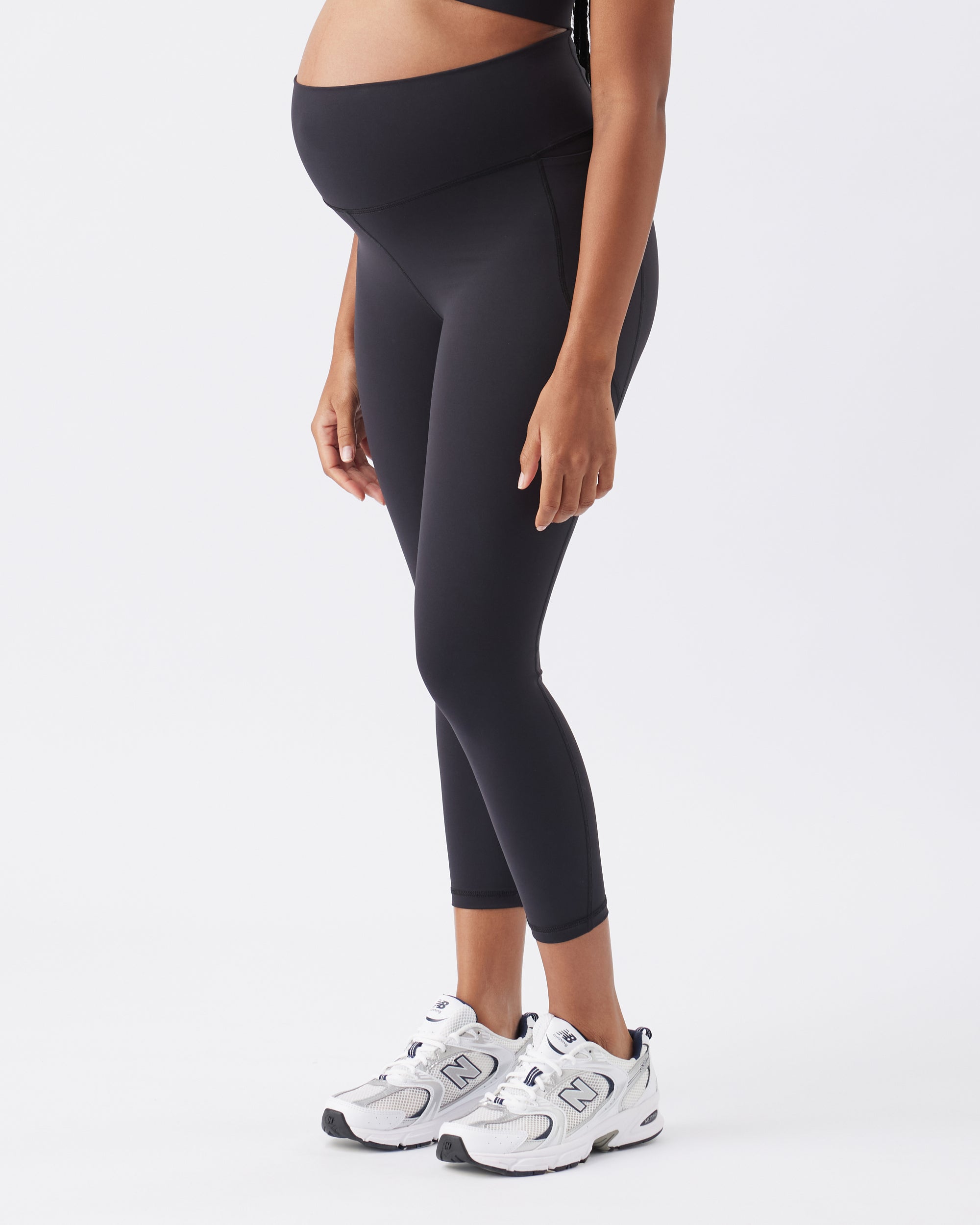 Pregnant women wearing black leggings and white sneakers on a white background