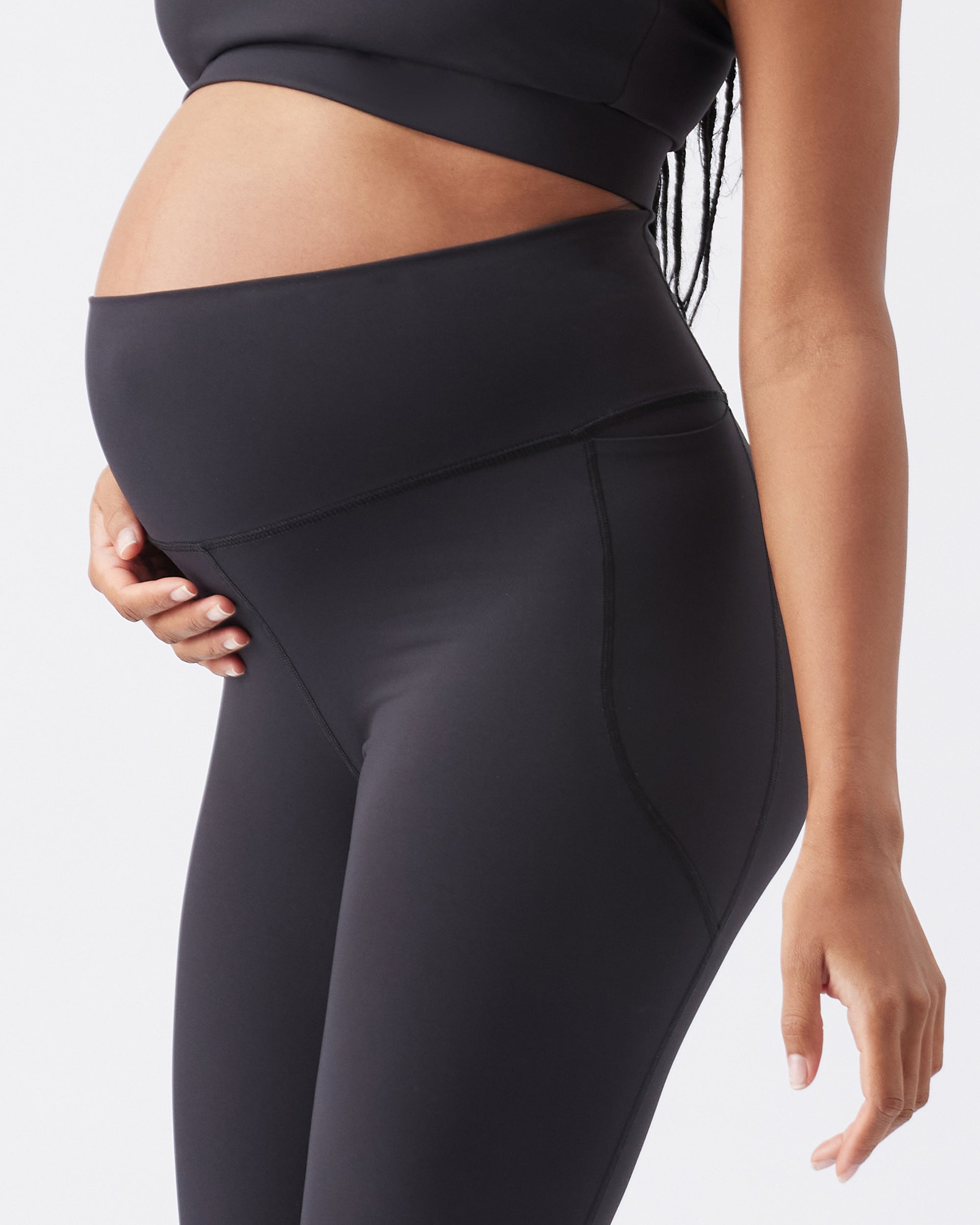 Pregnant woman wearing black maternity leggings on a light gray background