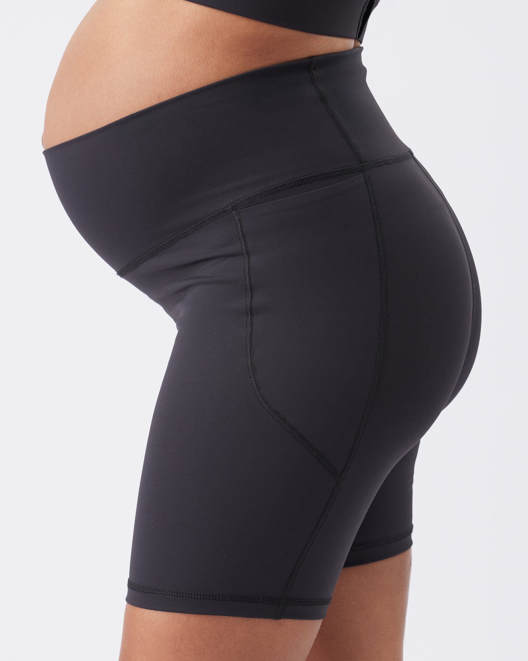 Black athletic shorts worn by a pregnant woman on a white background