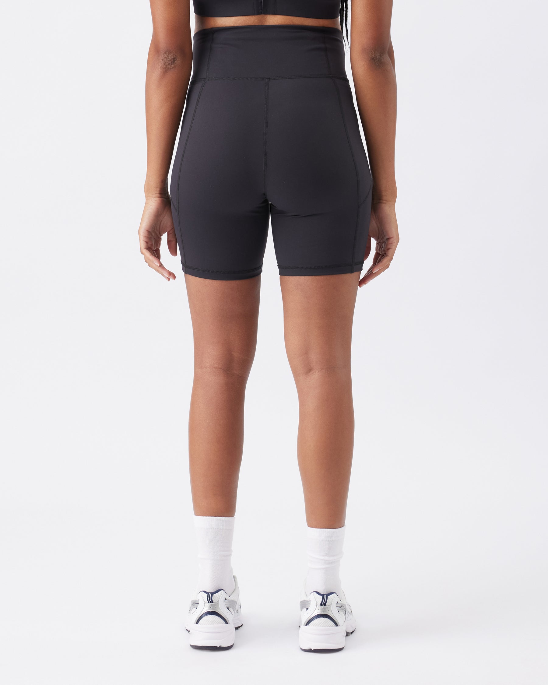 Back view of a woman wearing black athletic shorts on a white background