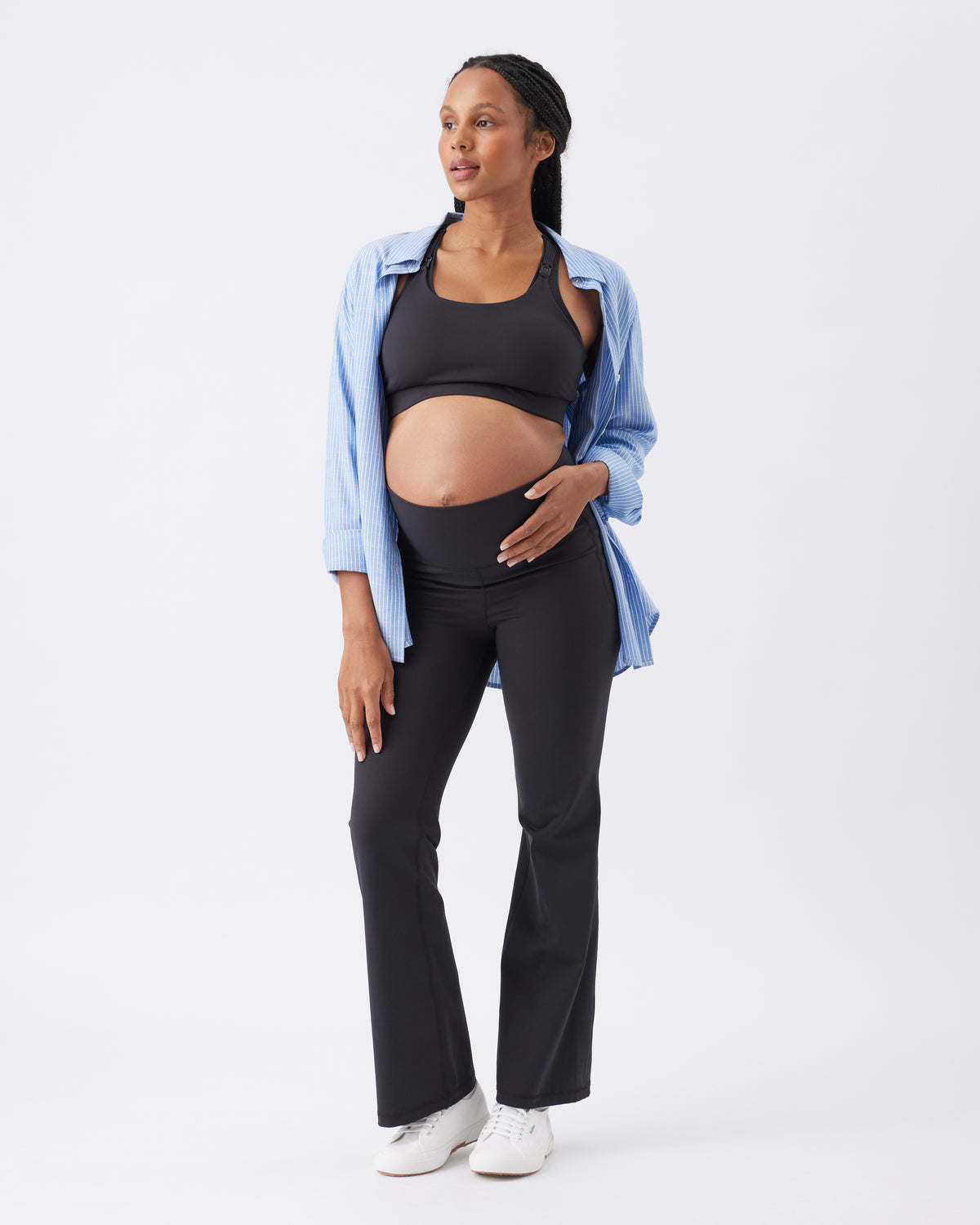Woman wearing a blue open shirt, black crop top and black active pants on a white background