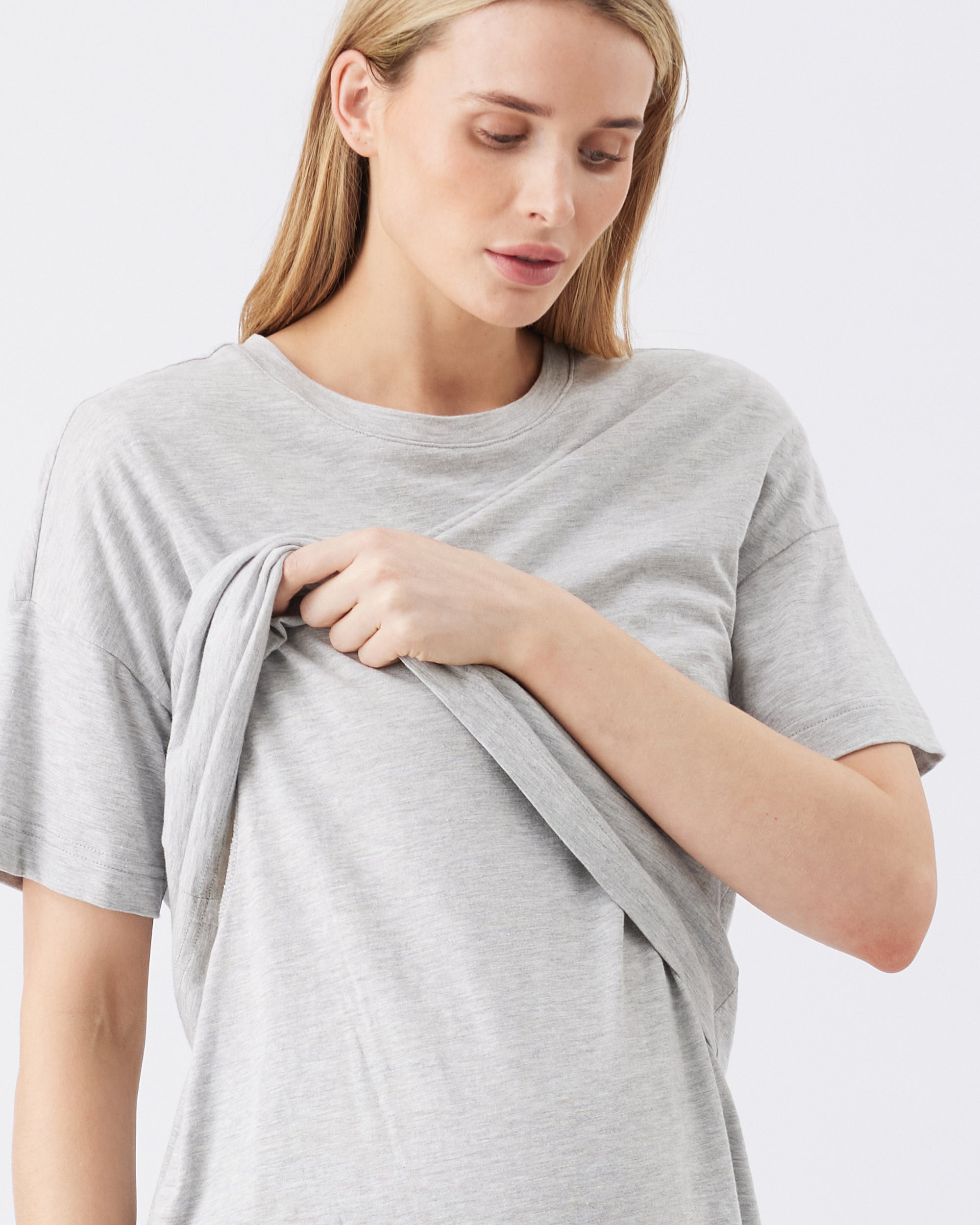 Woman wearing a gray nursing t-shirt against a white background. She is lifting up the nursing element