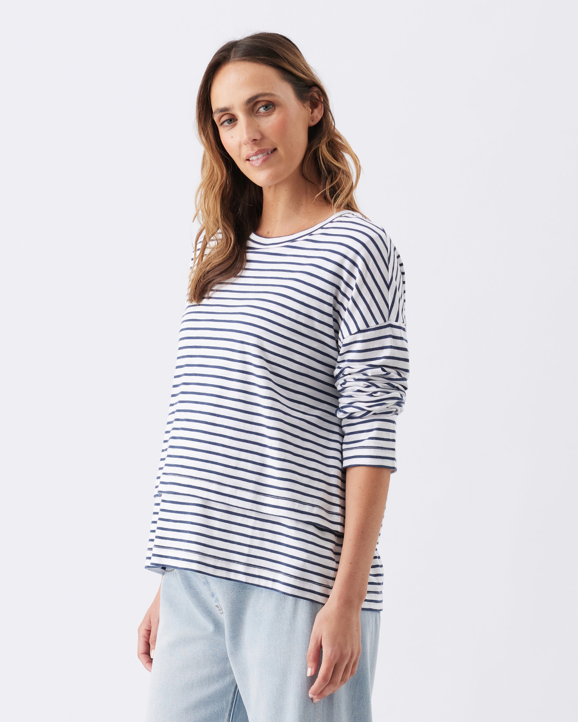 Woman wearing a striped shirt with the sleeves rolled up, with light blue jeans.