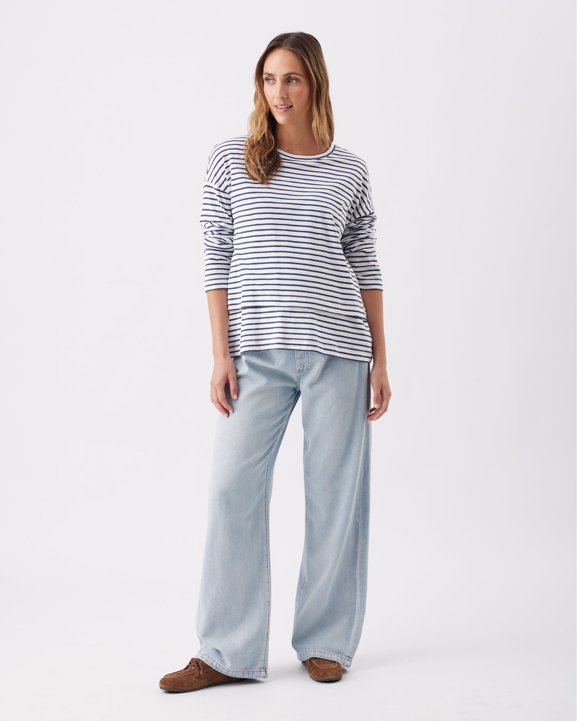 Full length shot of a pregnant woman wearing a striped long sleeve top and light blue pants on a white background