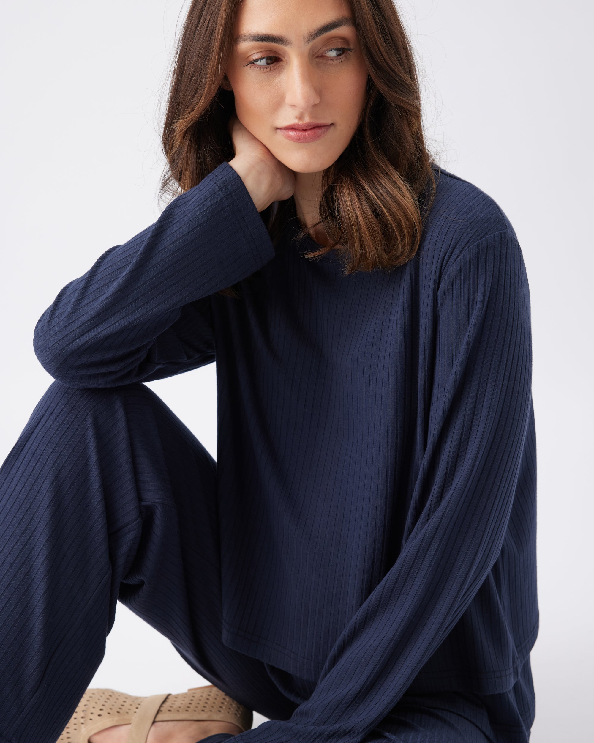 Woman sitting down wearing a navy blue long-sleeve top against a white background