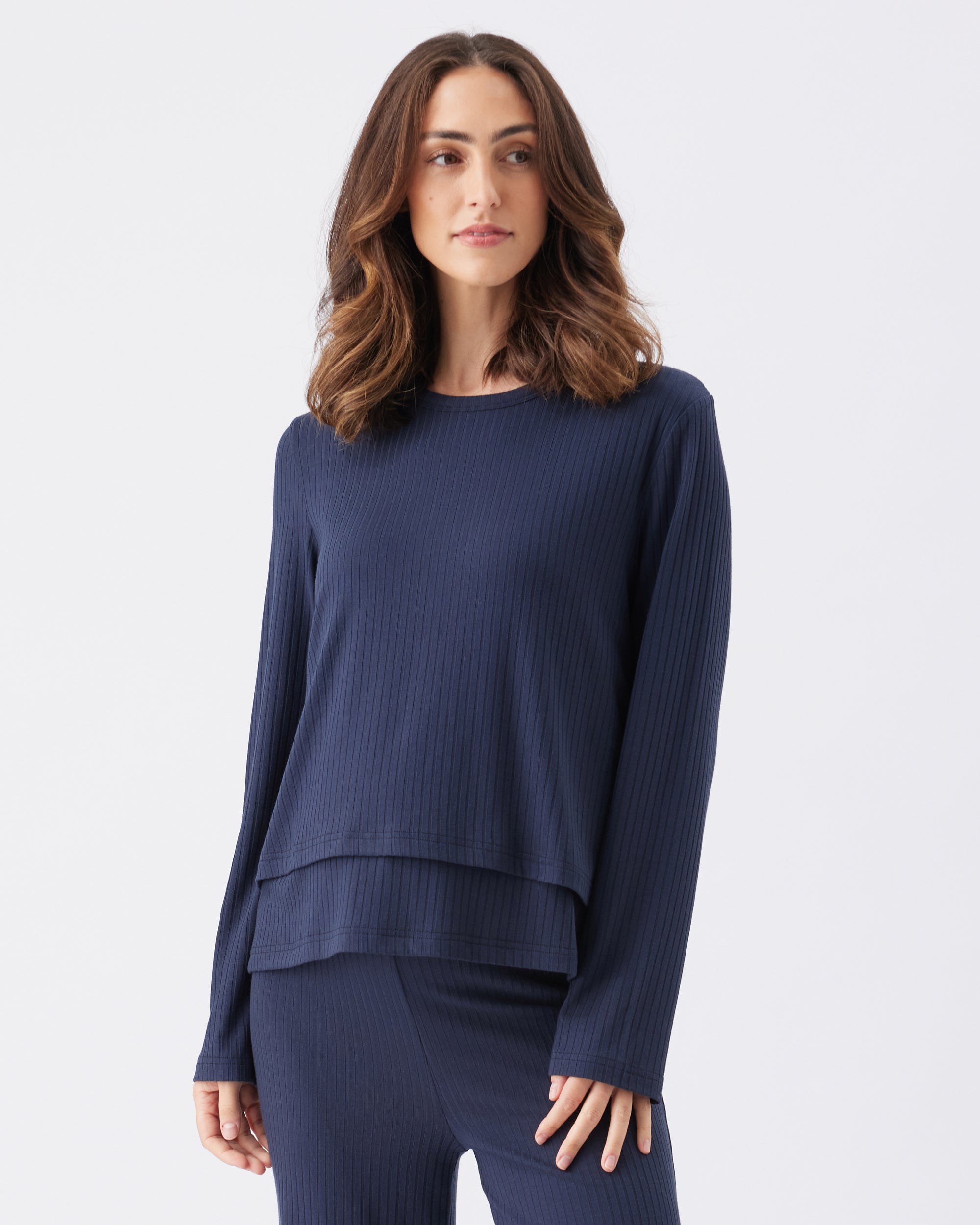 Woman wearing a navy blue ribbed sweater and pants on a light gray background