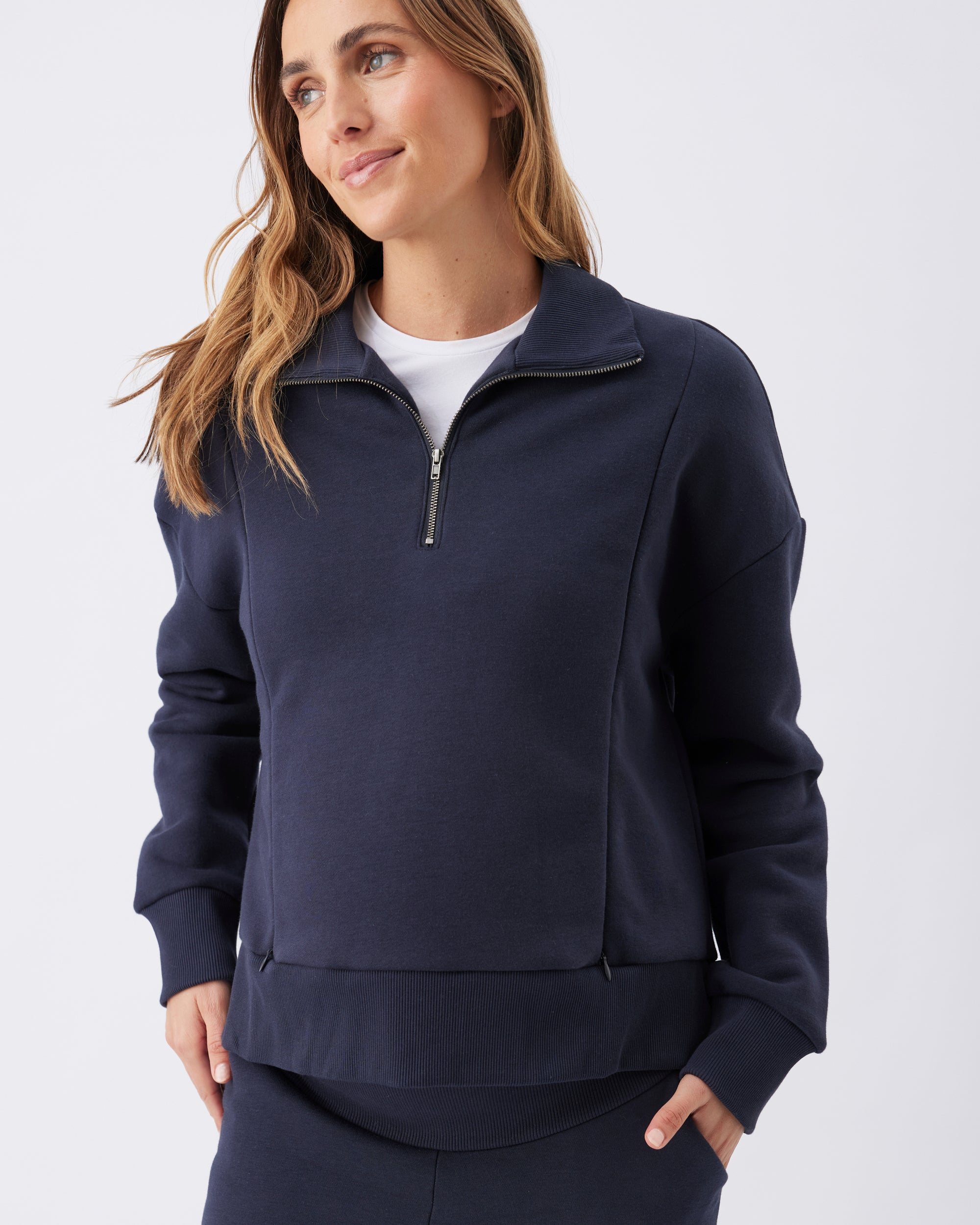 Woman wearing a navy blue zip-up nursing friendly sweatshirt from Ripe Maternity