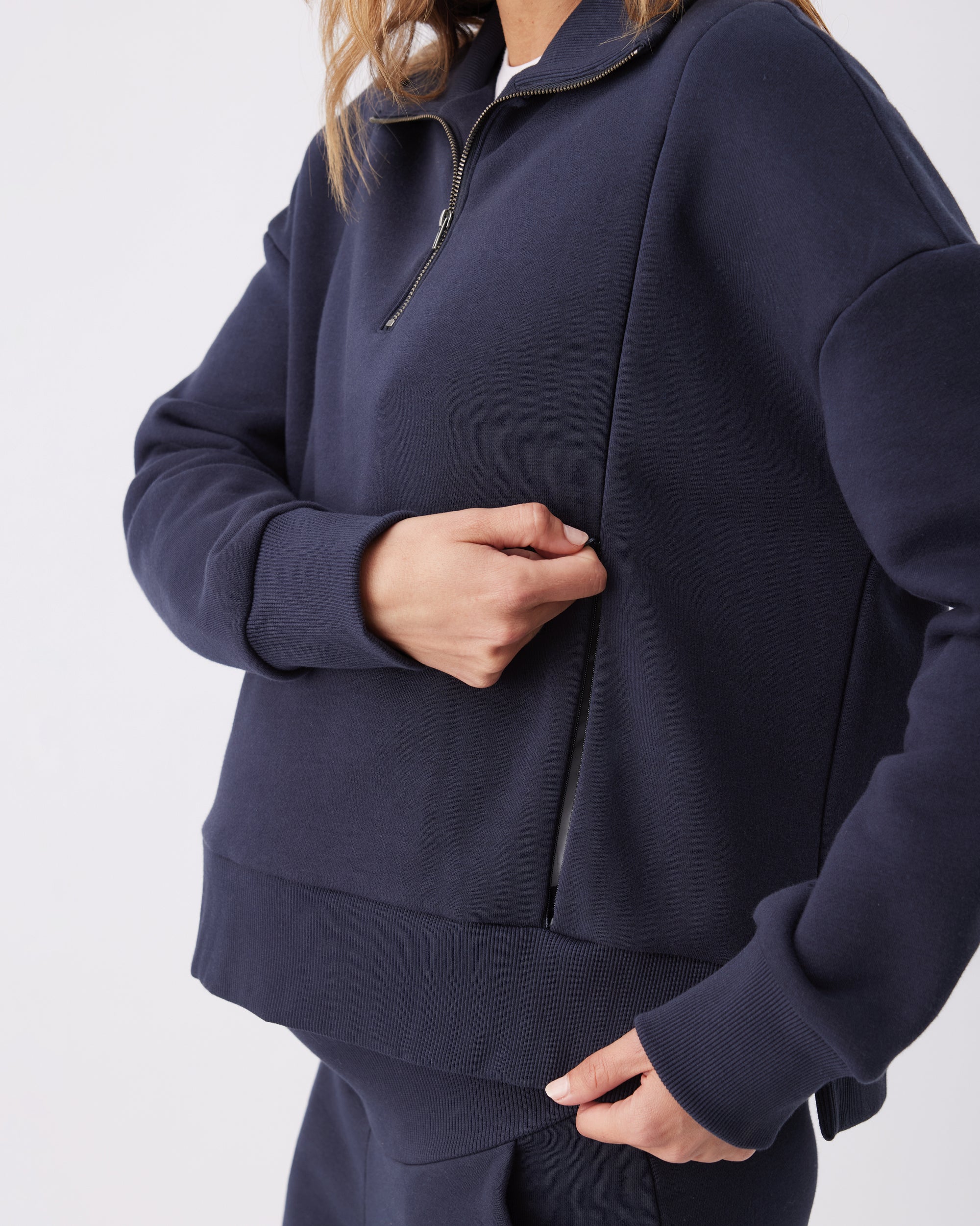 Side view of a  woman unzipping the nursing access on a navy blue tracksuit top.